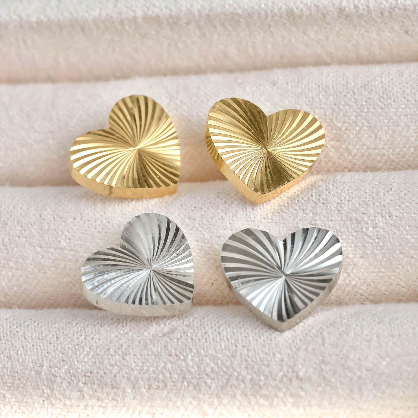 Gold and silver heart-shaped earrings on a textured white surface