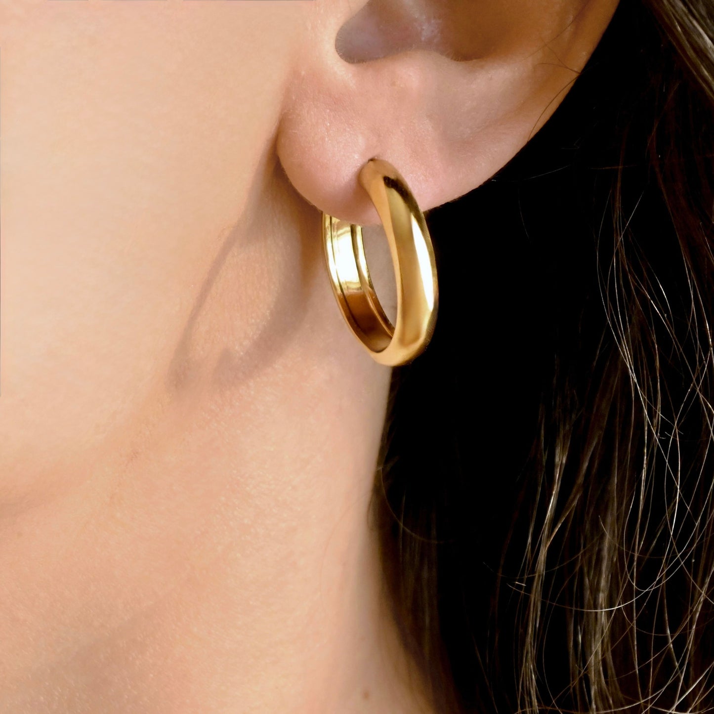 A close-up of a person's ear wearing a polished gold hoop earring.