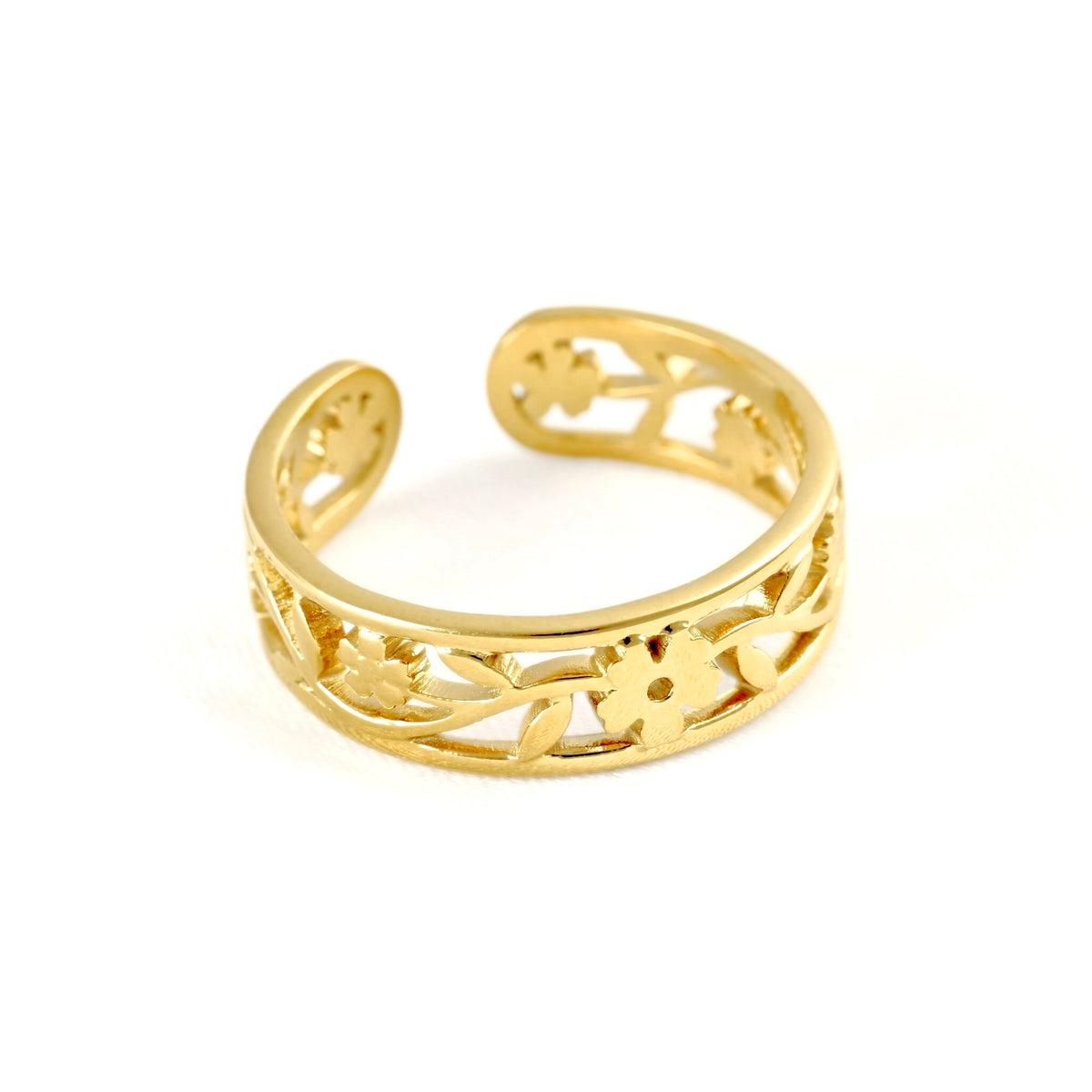 Wide gold cuff ring with open back and rounded ends, and filigree pattern on white surface.