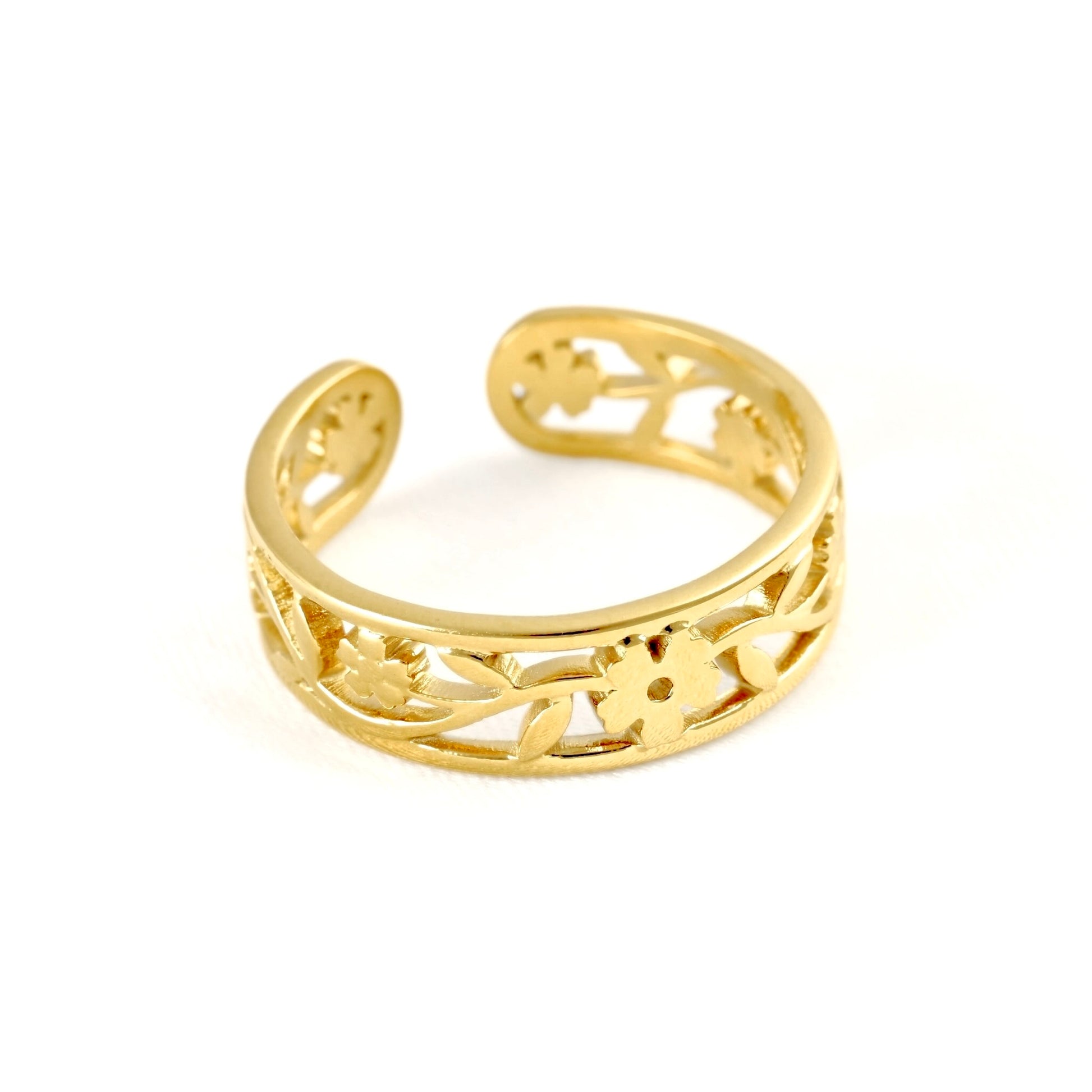 Wide gold cuff ring with open back and rounded ends, and filigree pattern on white surface.