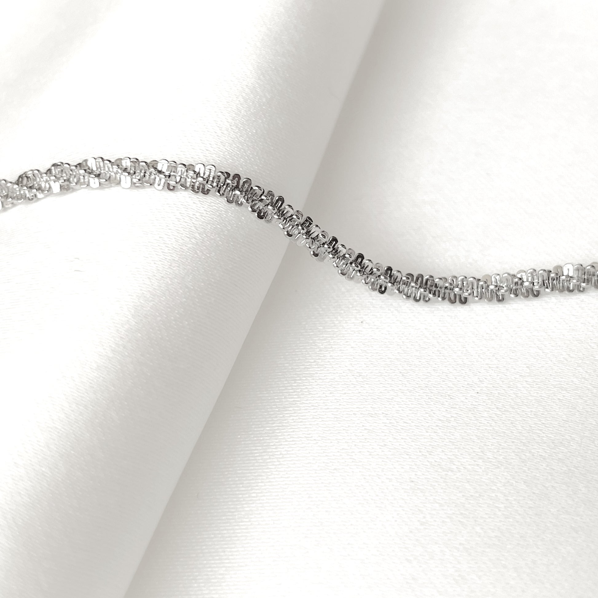 Side view of silver sparkle rope bracelet on a white fabric background