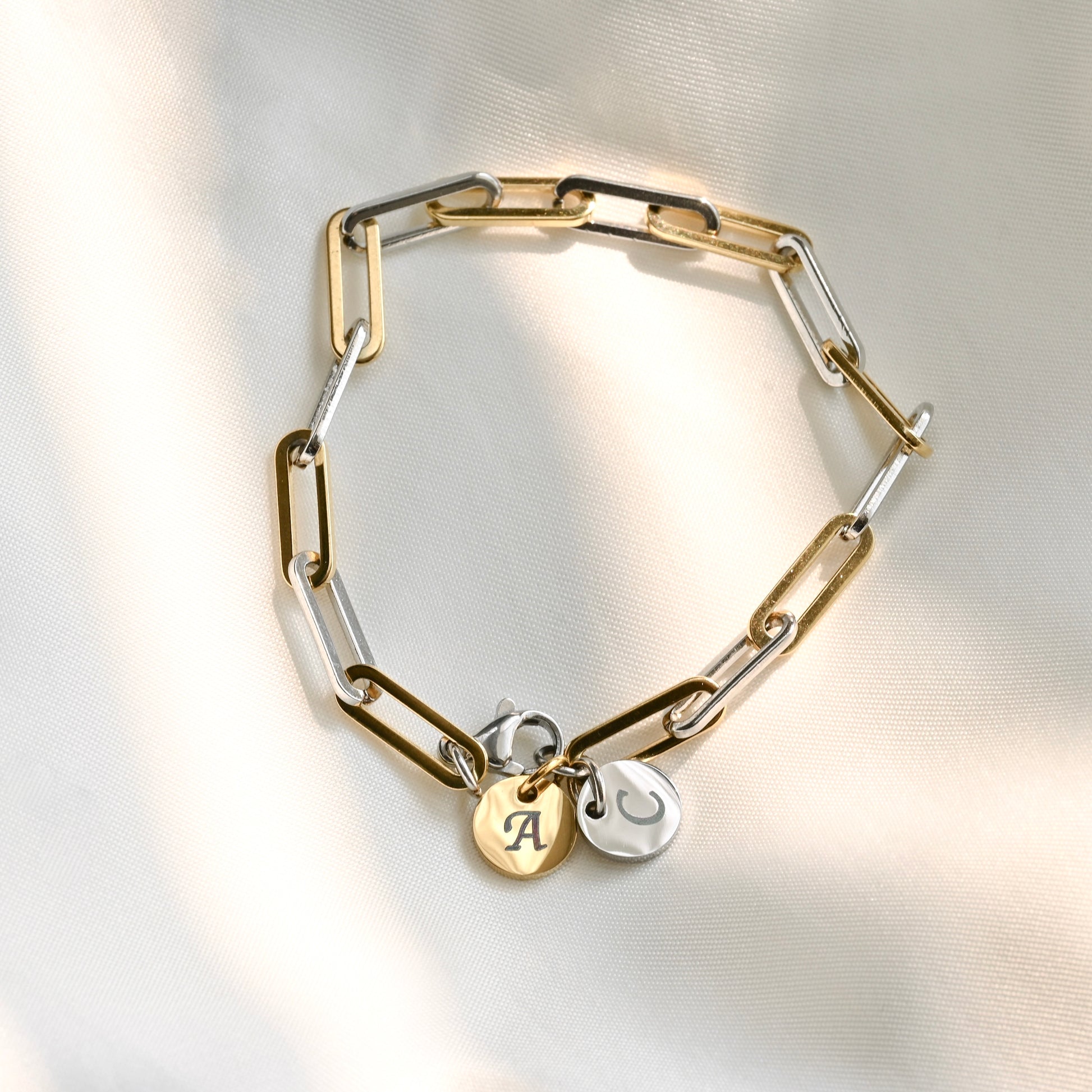 two tone thick paperclip chain bracelet with round two tone charms on a light background