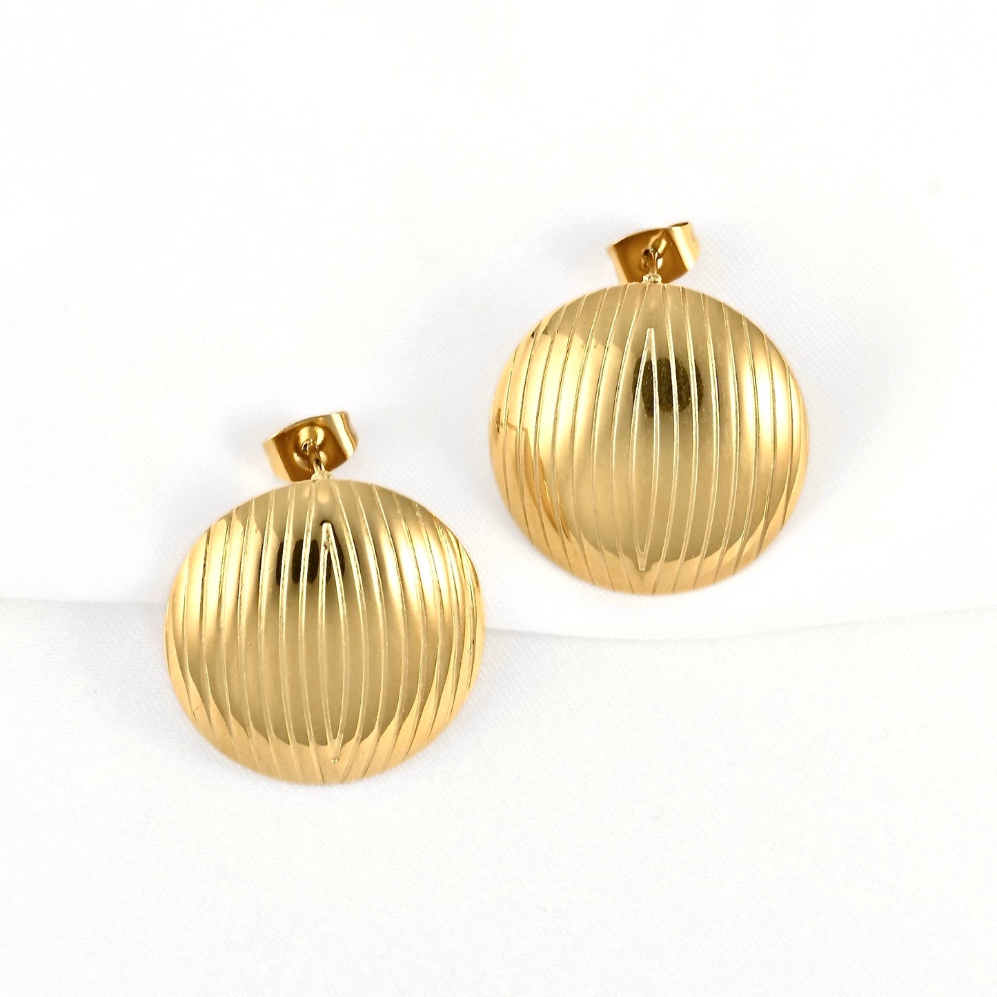 A pair of round gold-tone earrings with a vertically ribbed texture, displayed on a clean white background.