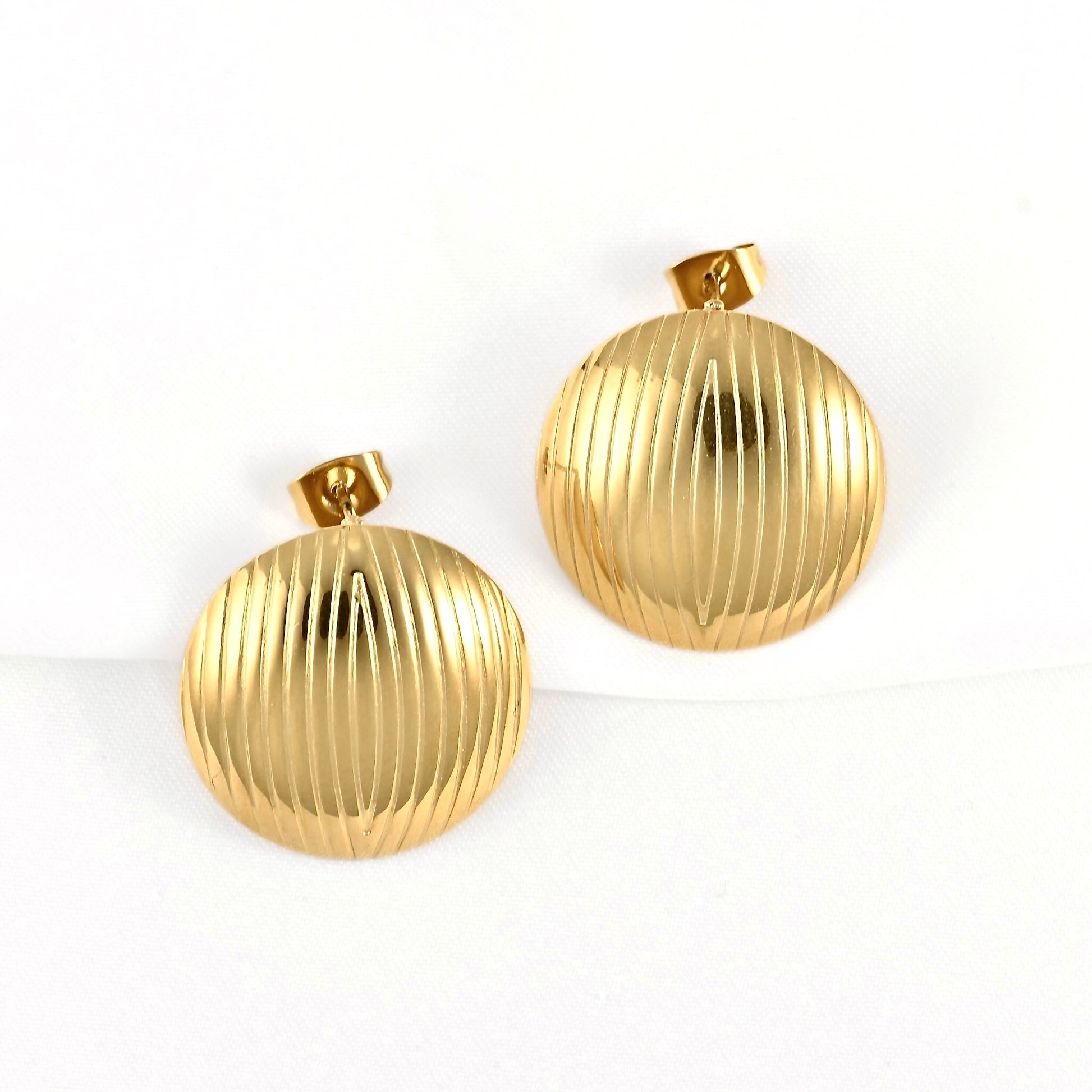 A pair of round gold-tone earrings with a vertically ribbed texture, displayed on a clean white background.