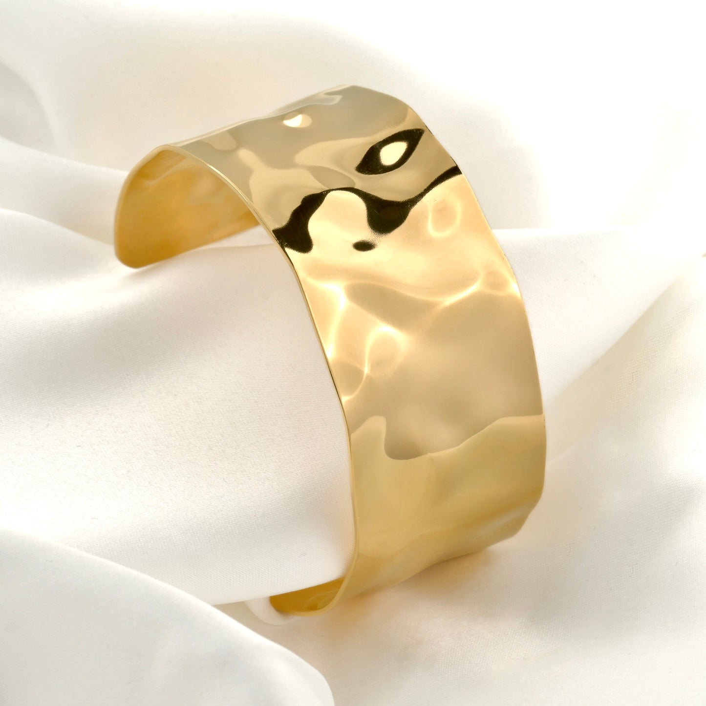 Textured gold open bangle on a white fabric background