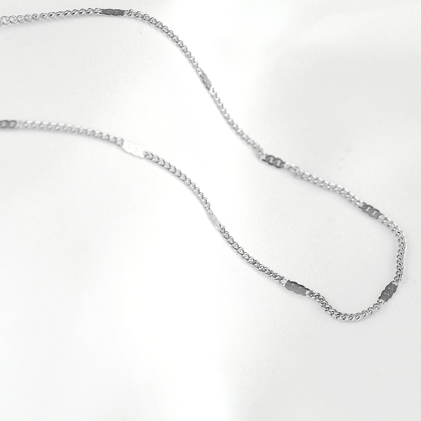 A silver-toned chain necklace with a flat, polished finish and small rectangular links, displayed on a clean white background.