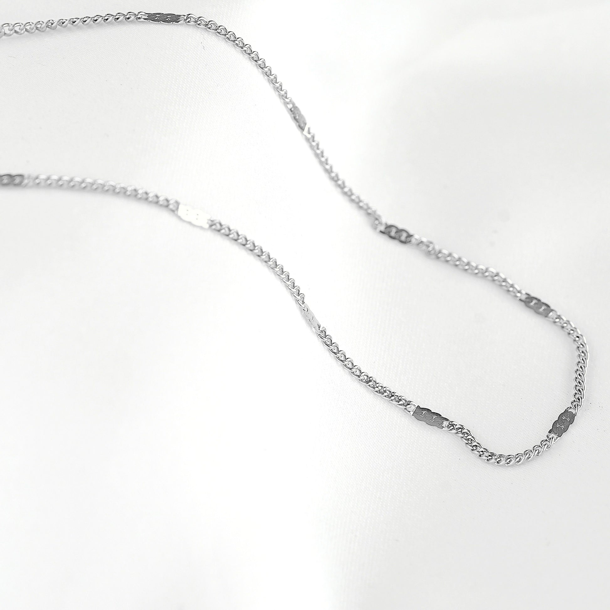 A silver-toned chain necklace with a flat, polished finish and small rectangular links, displayed on a clean white background.