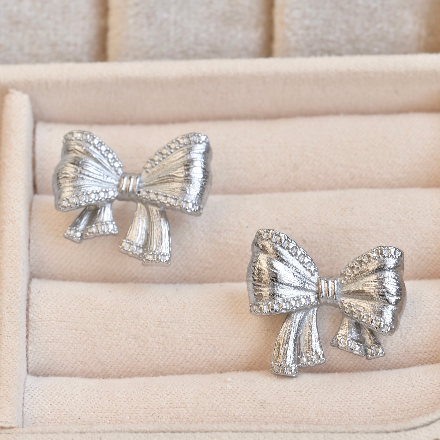Silver bow tie earrings on a beige jewelry cushion