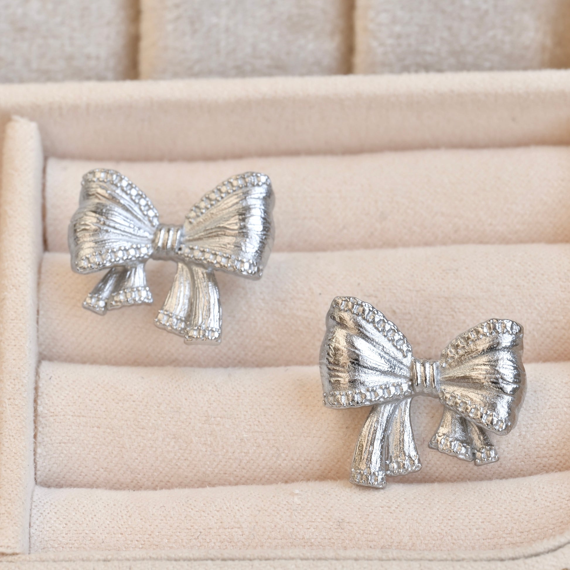 Silver bow tie earrings on a beige jewelry cushion
