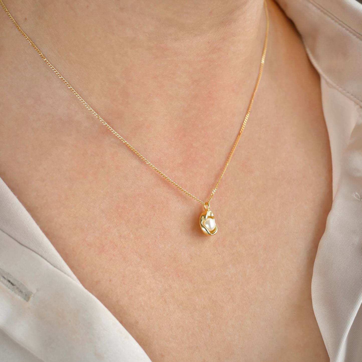 Gold necklace with pearl charm on a person wearing a white blouse.