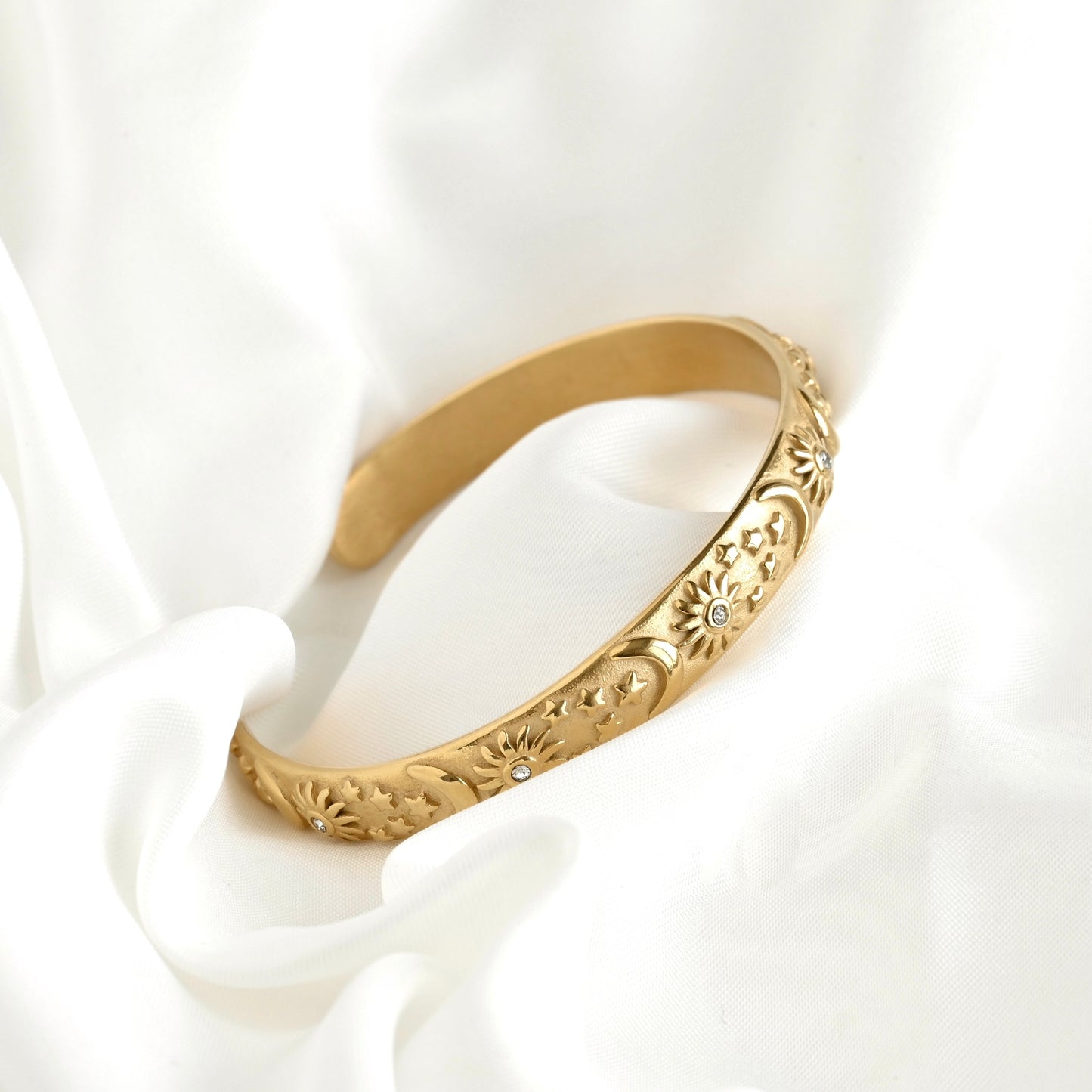 Gold sun bracelet on a white fabric background