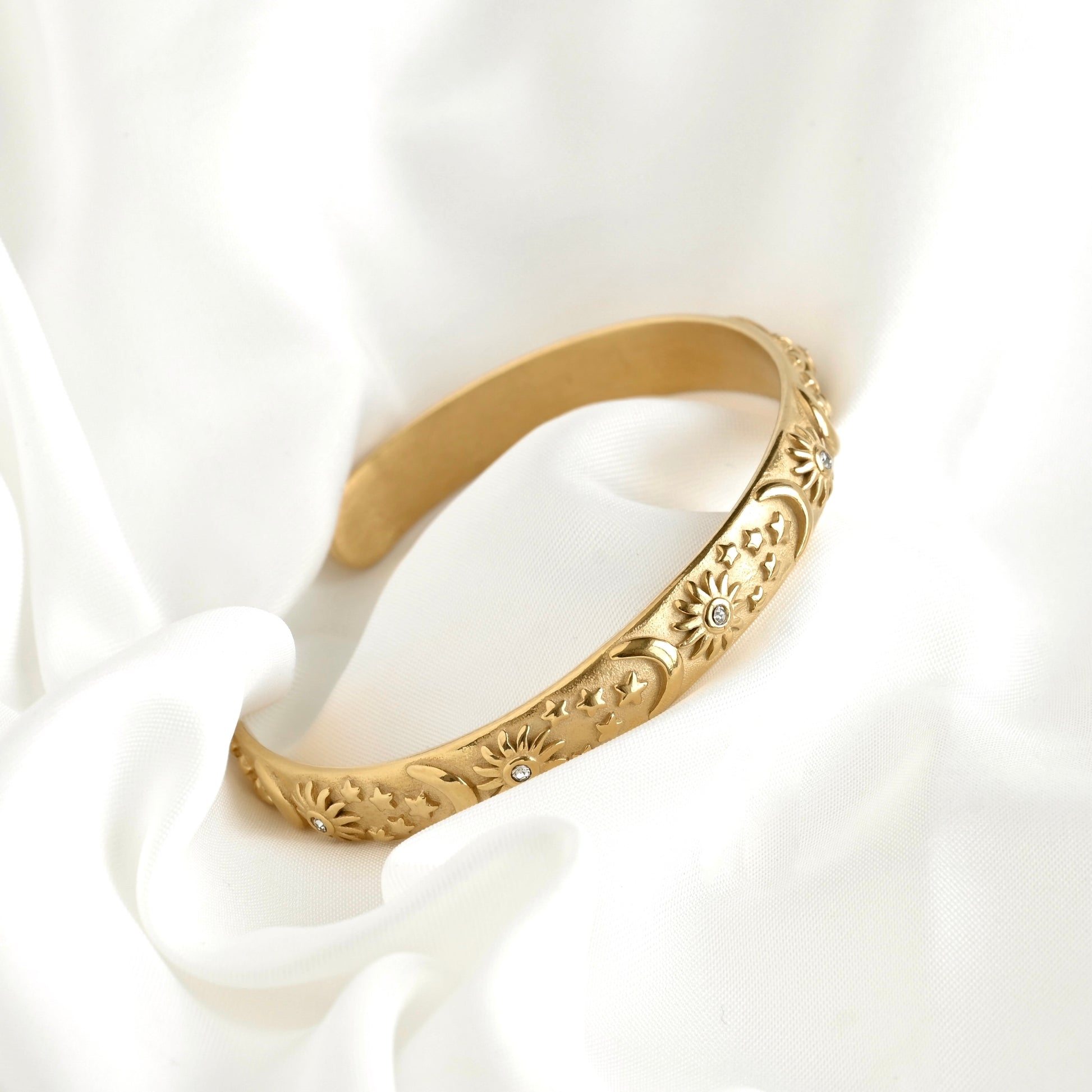 Gold sun bracelet on a white fabric background
