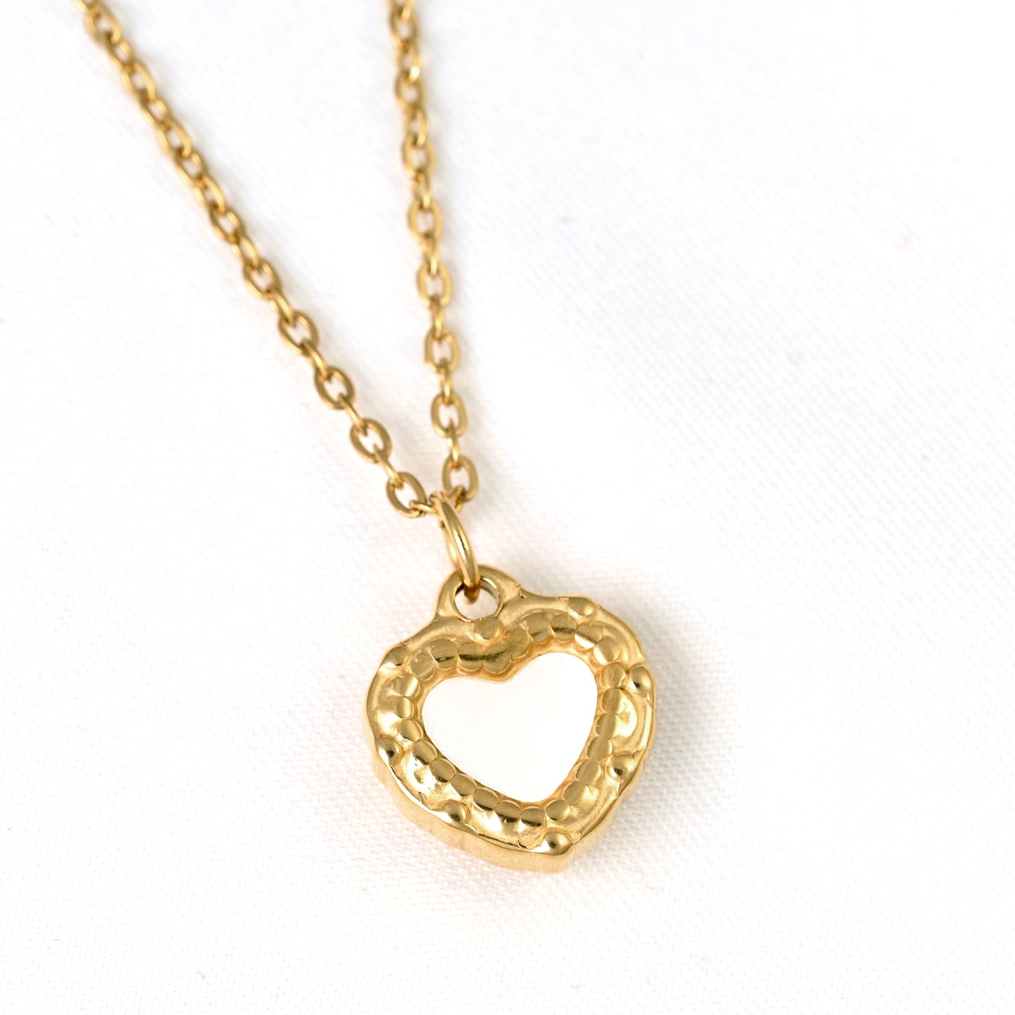 A gold heart-shaped pendant necklace with a textured, hammered finish on the outer border and a smooth inner heart, shown on a white background.