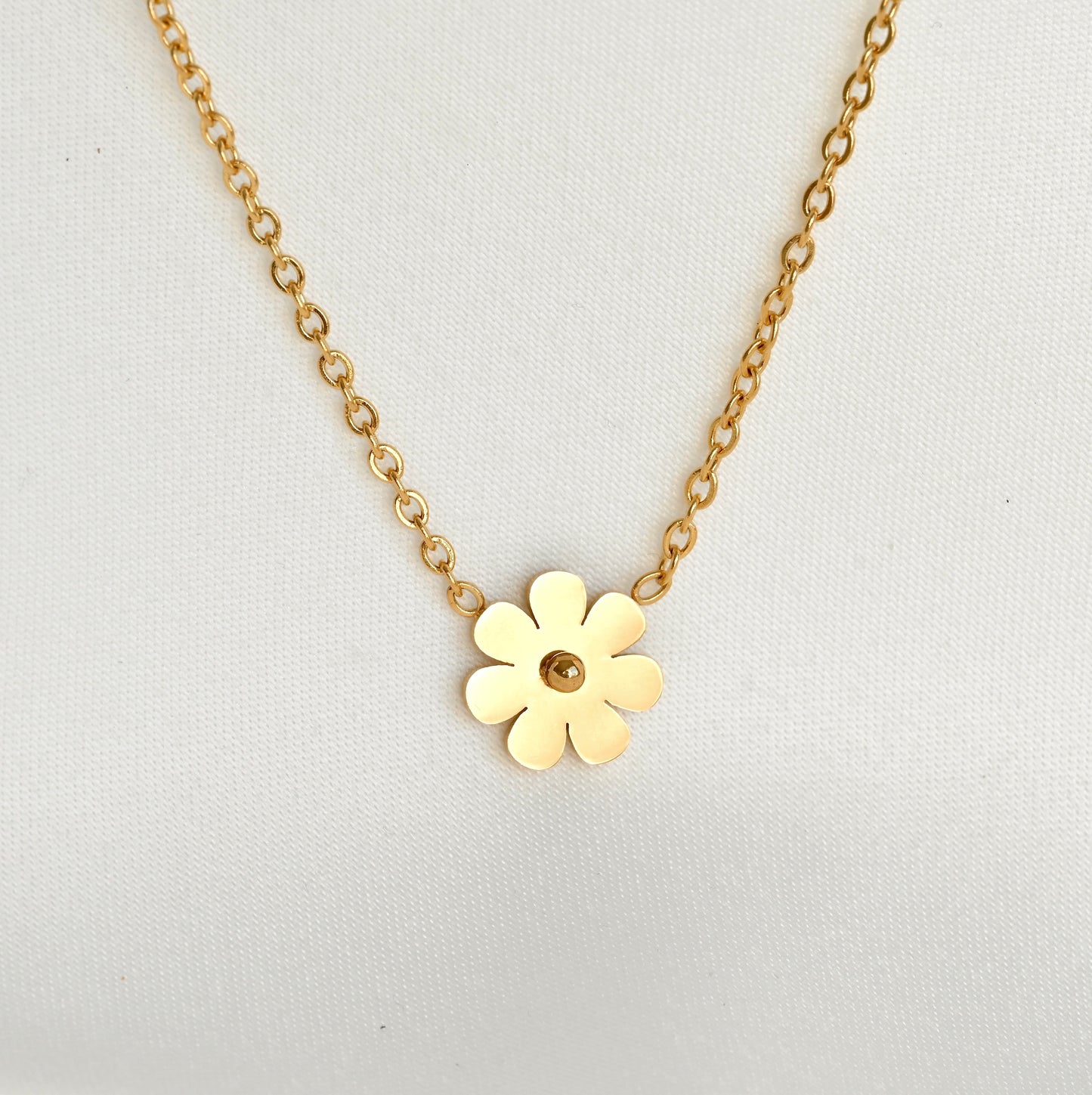 Front-view of gold flower necklace with the flower charm fully reflecting light on a light gray background