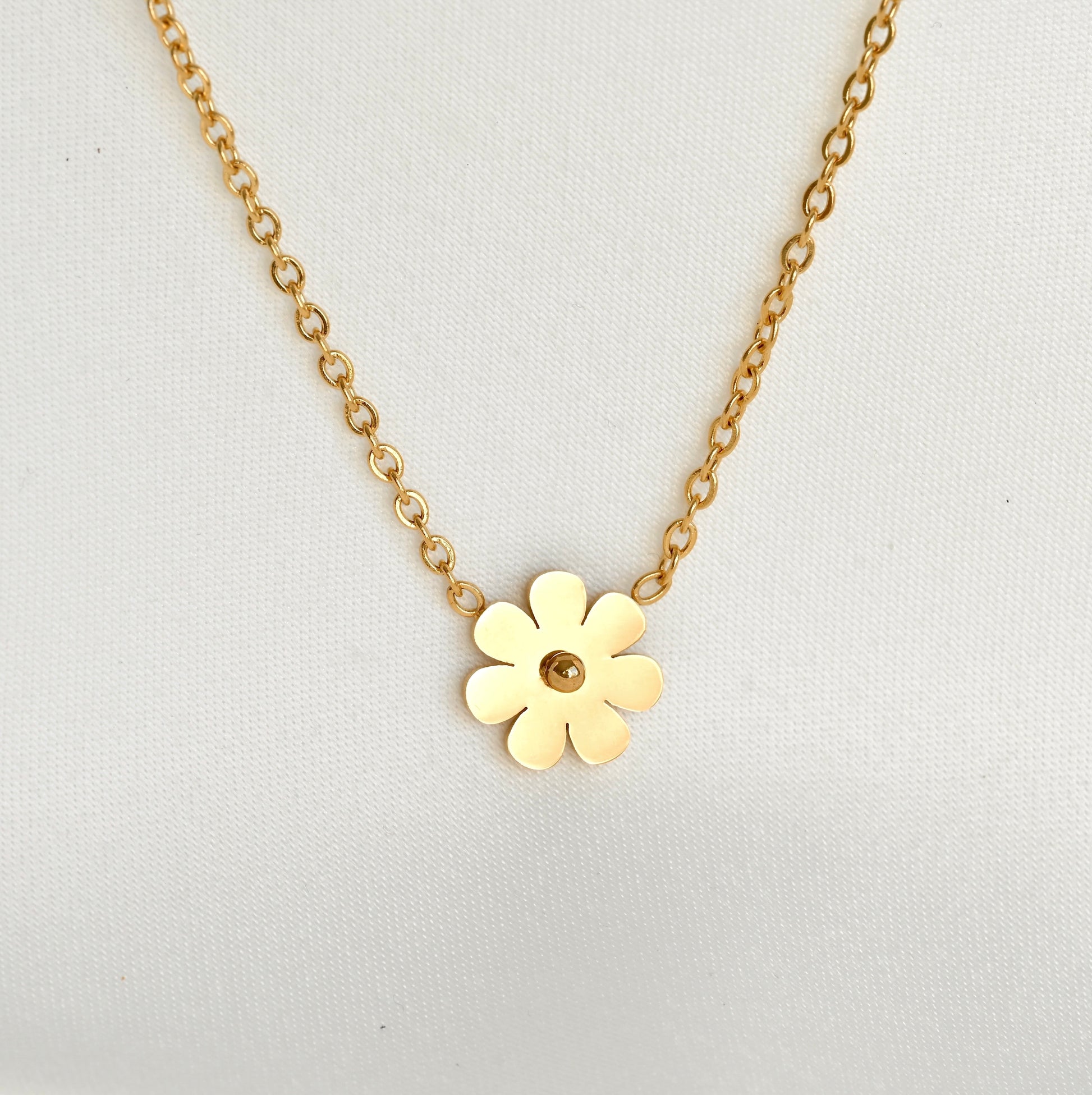 Front-view of gold flower necklace with the flower charm fully reflecting light on a light gray background