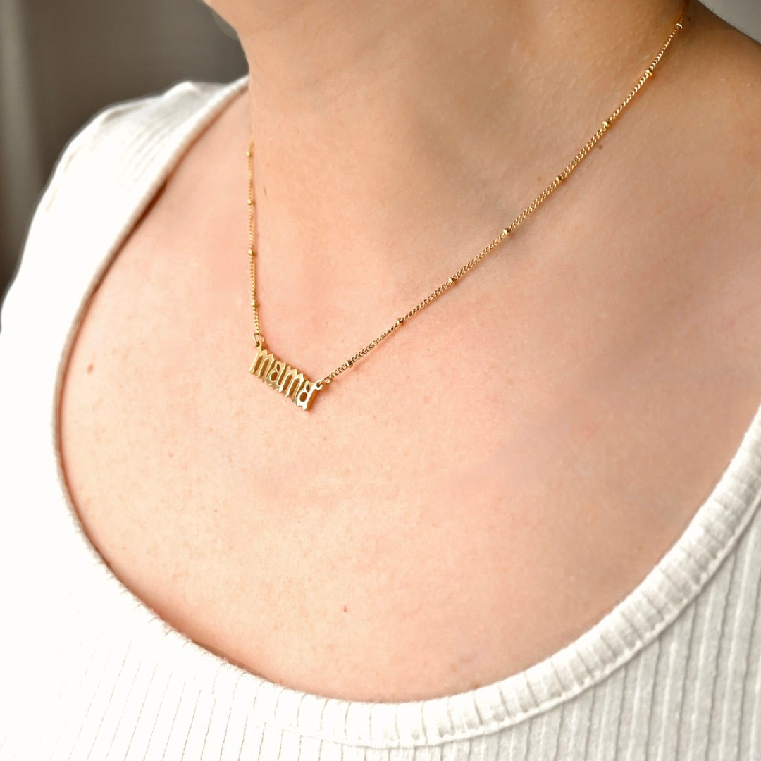 Gold satellite necklace with 'mama' pendant on a person wearing a white top.