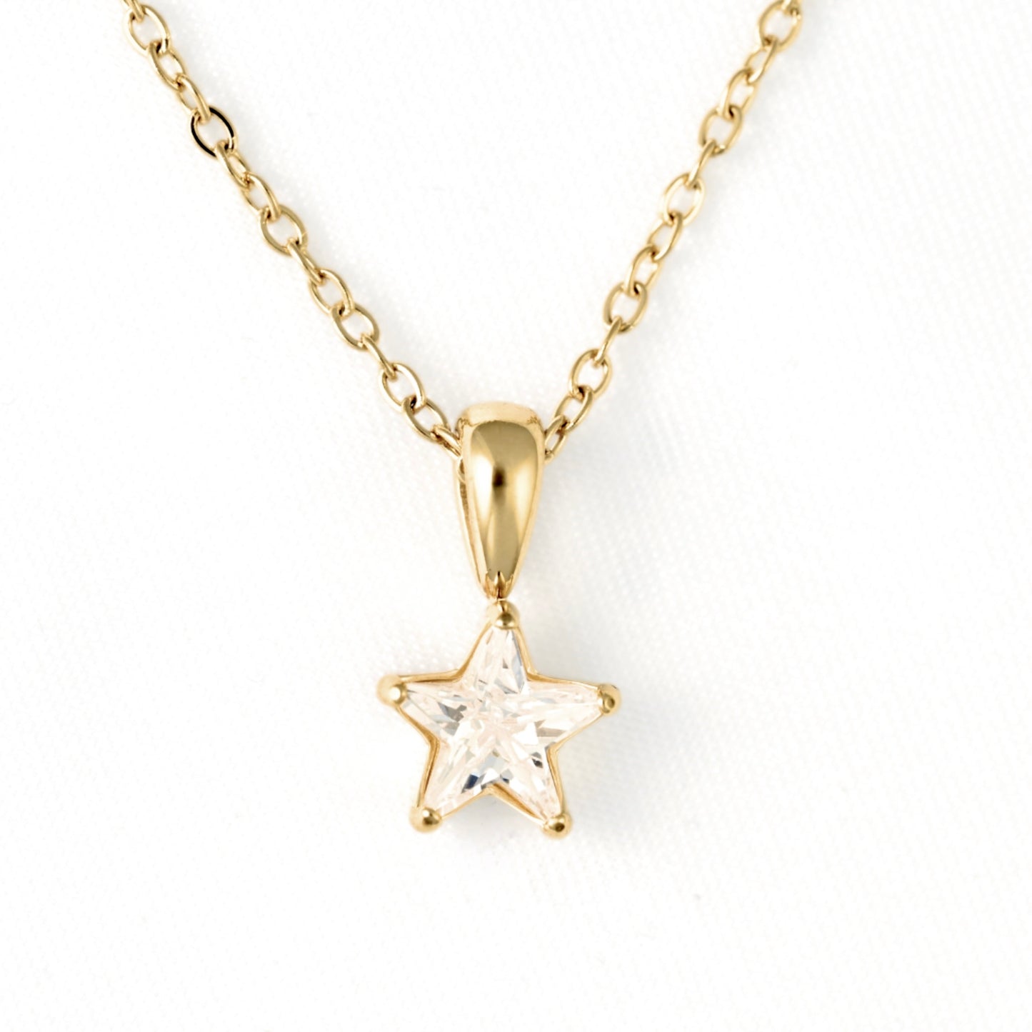 A gold star pendant necklace with a clear faceted gemstone, suspended from a delicate gold chain on a white background.