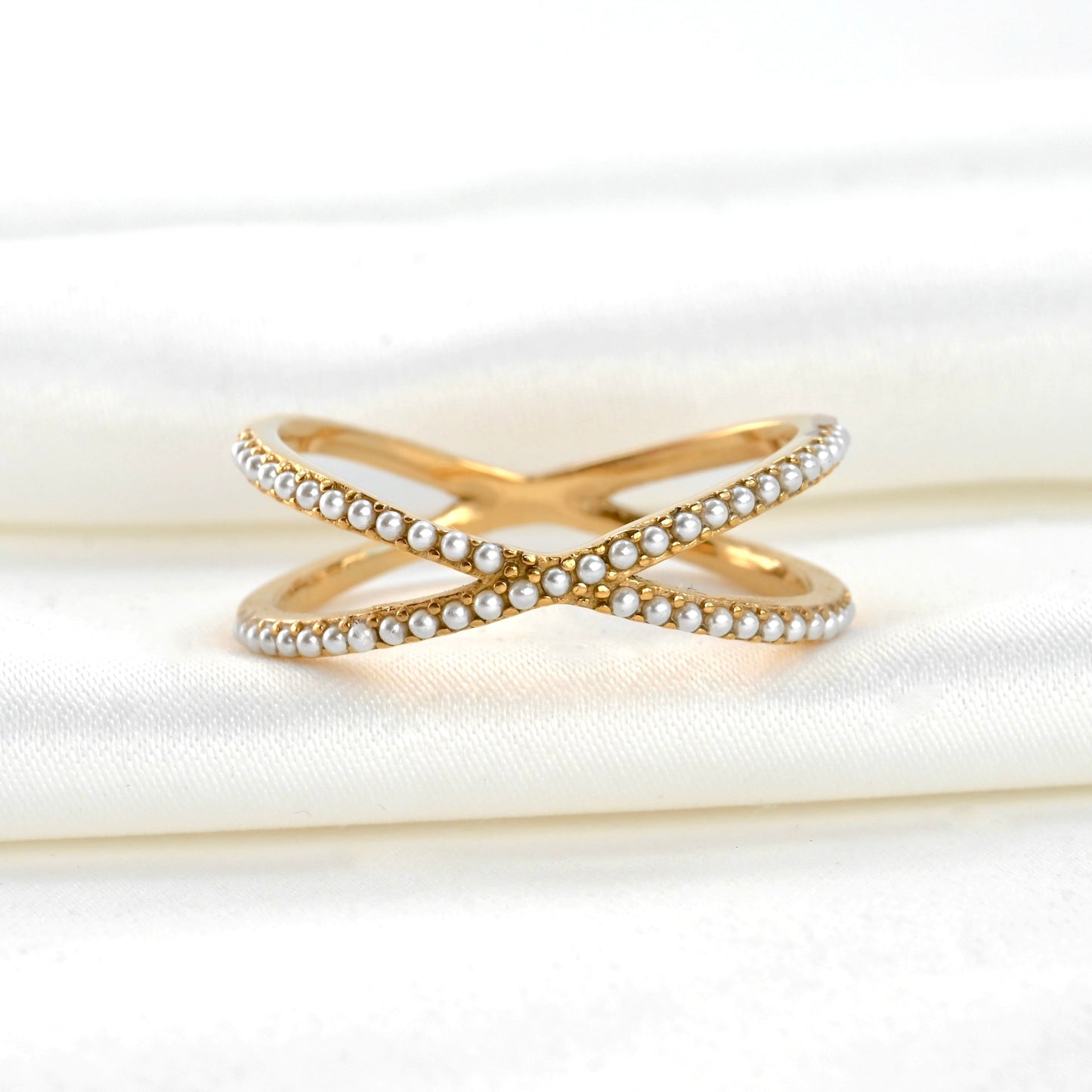 Gold criss cross ring with pearl accents on a white fabric background