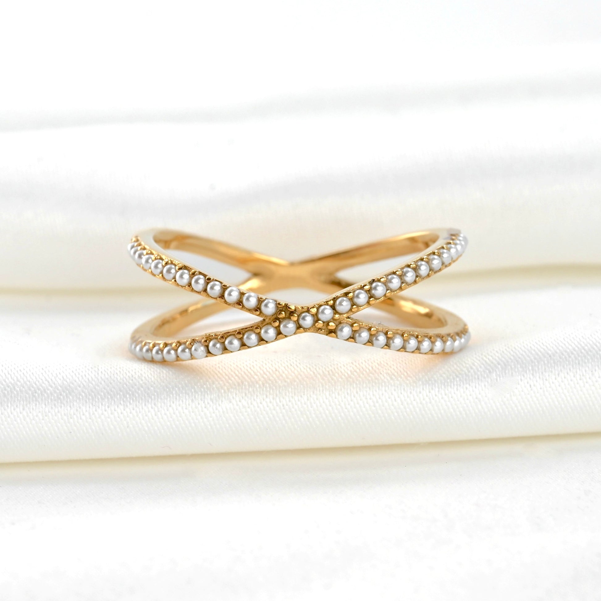 Gold criss cross ring with pearl accents on a white fabric background