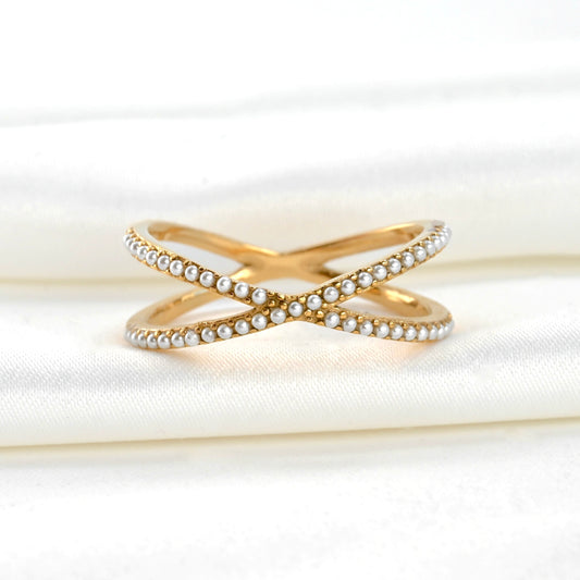 Gold criss cross ring with pearl accents on a white fabric background