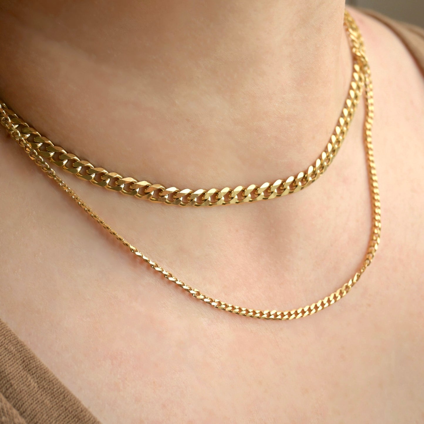 Two Gold cuban link chains layered on a person's neck