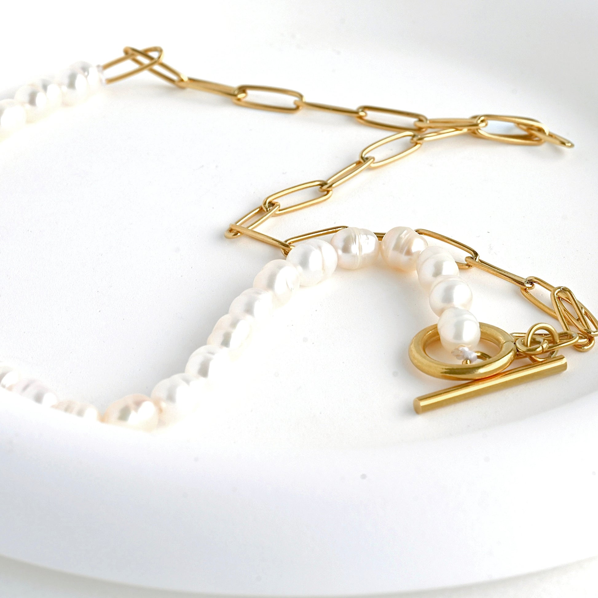 Gold paperclip and baroque pearl chain necklace on a white background