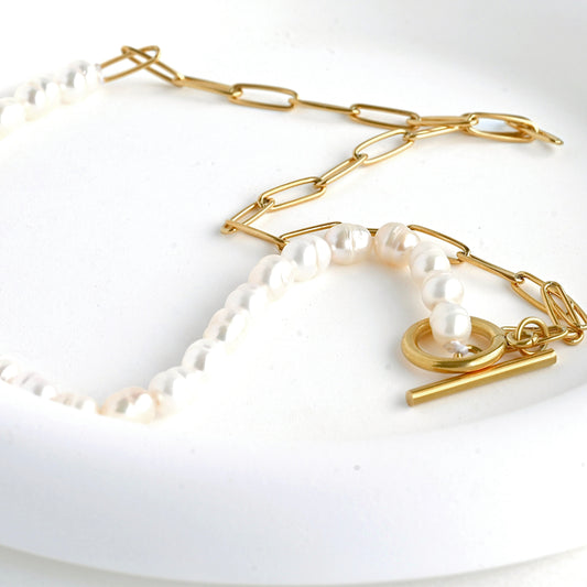 Gold paperclip and baroque pearl chain necklace on a white background