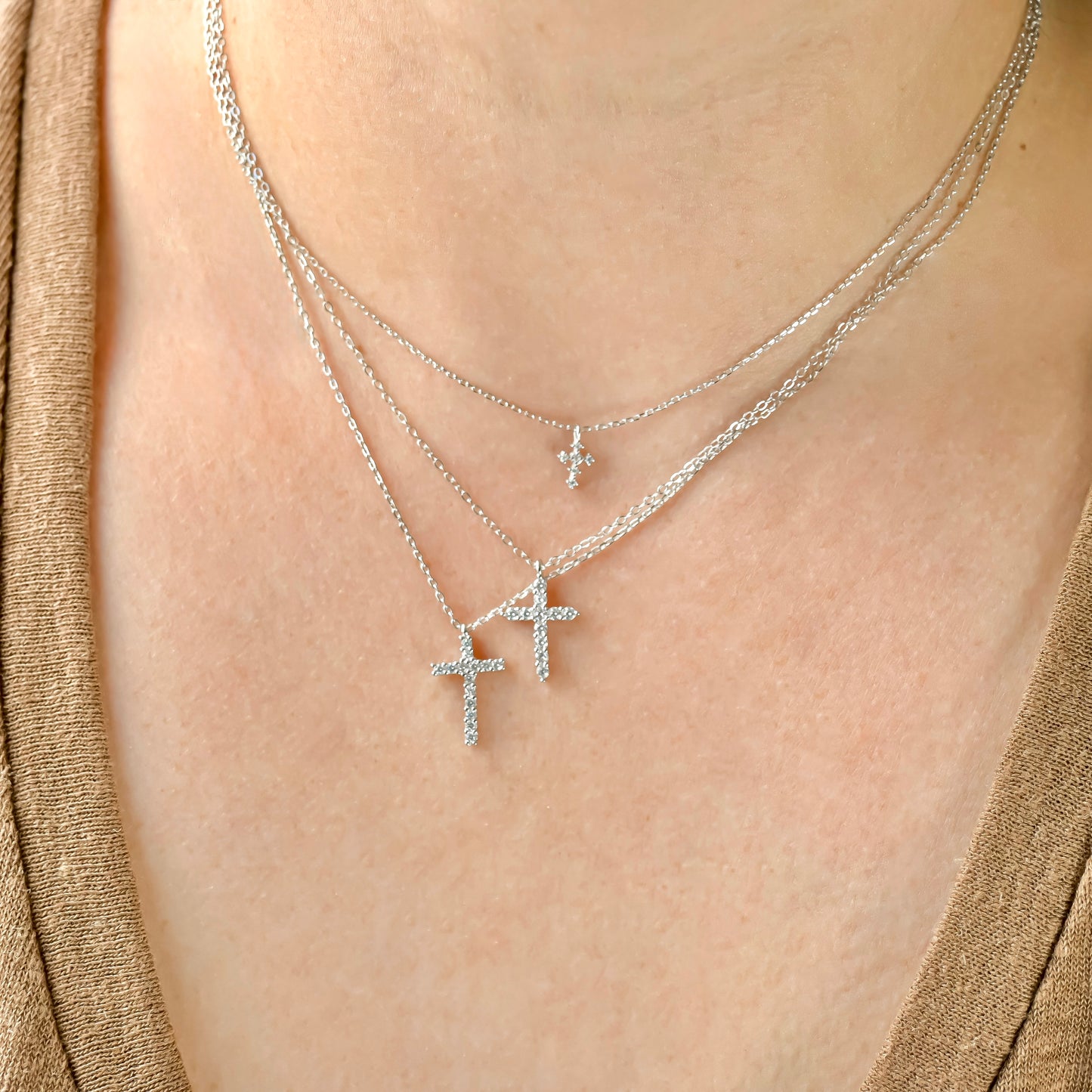 Layered silver diamond cross necklaces with thfree different sizes on a person wearing a gold top.