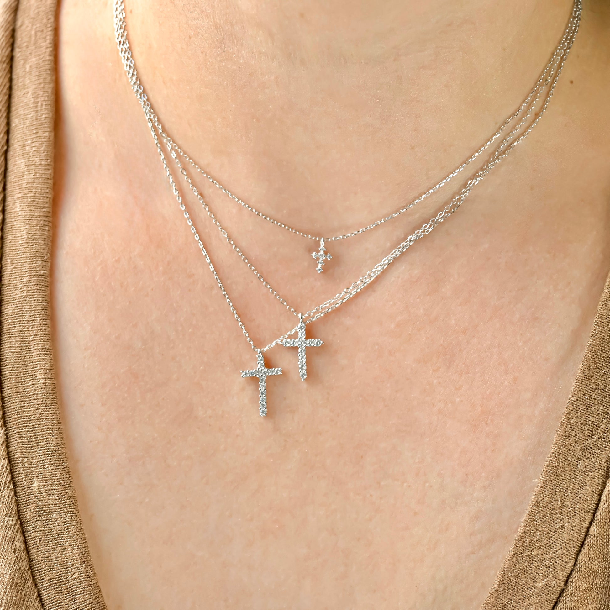 Layered silver diamond cross necklaces with thfree different sizes on a person wearing a gold top.