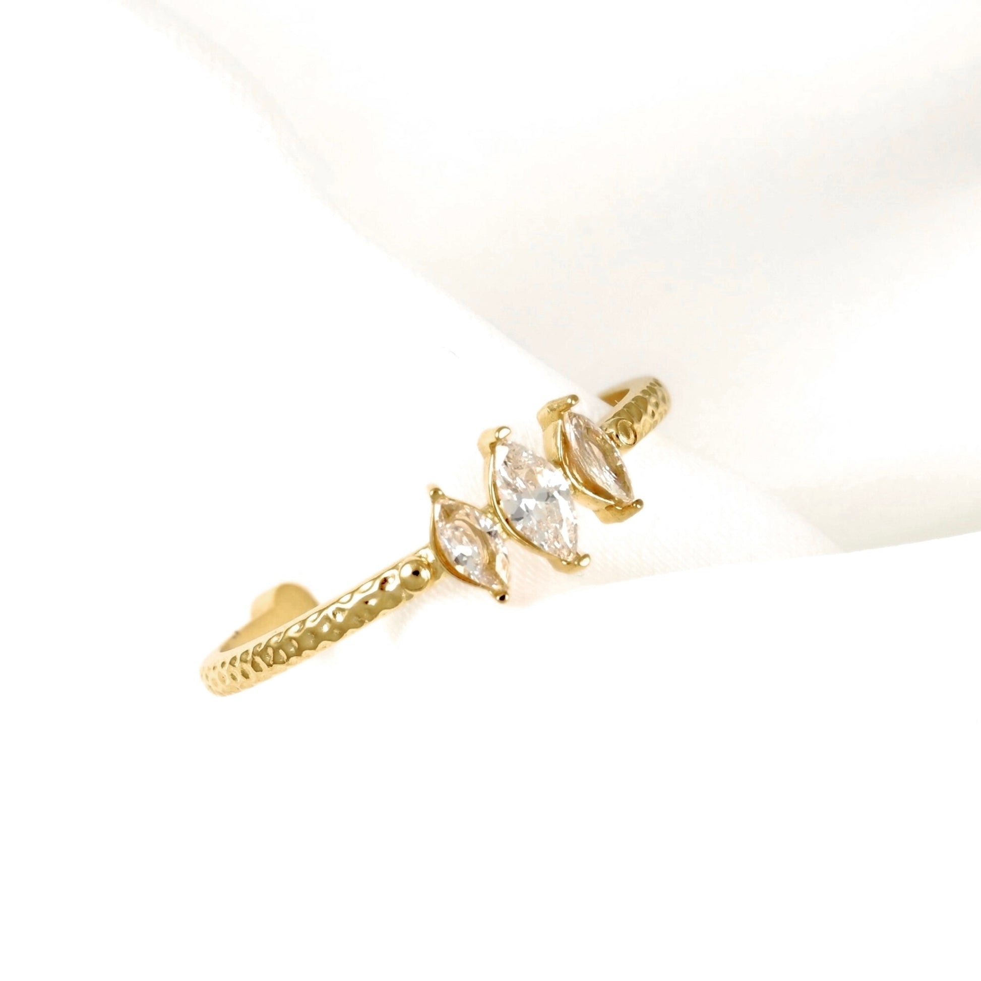 A gold ring with three marquise-cut clear gemstones set in a textured band, displayed on a soft white background.