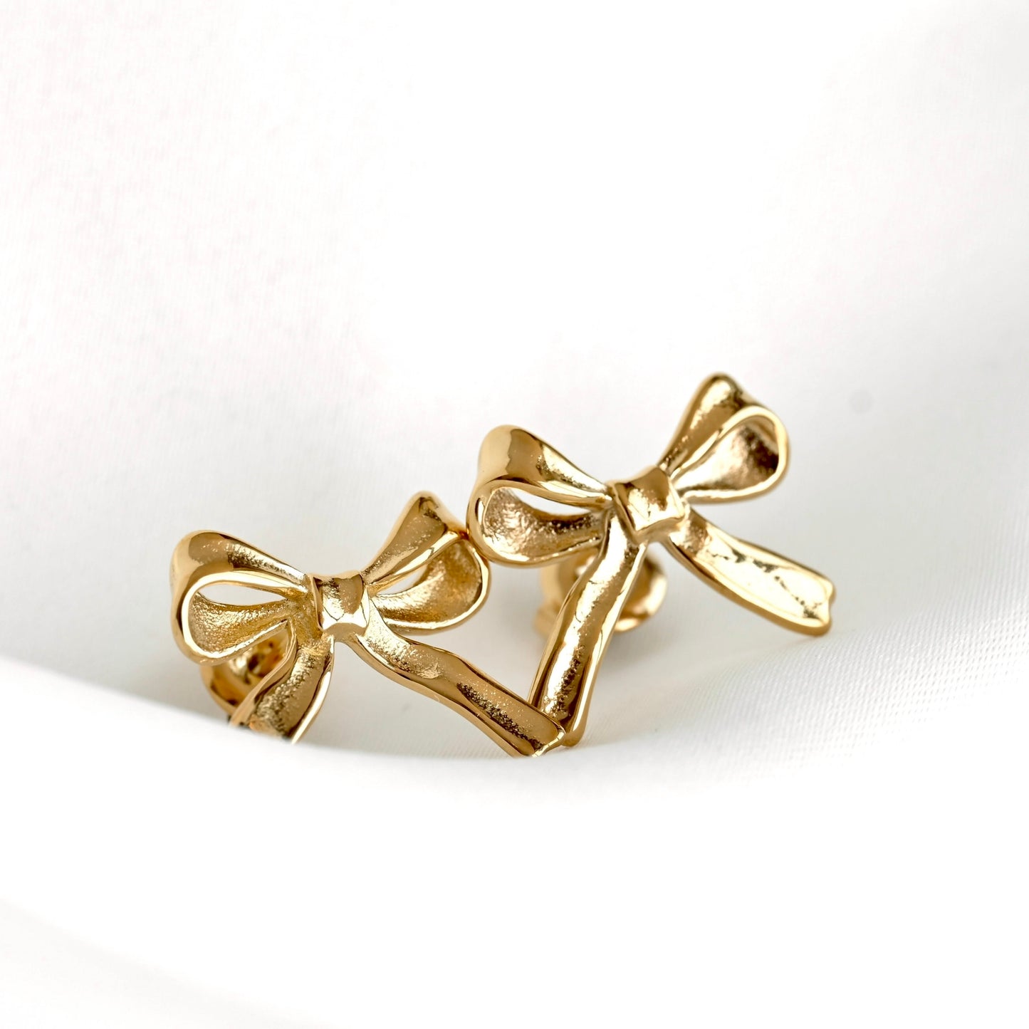 A pair of gold bow drop earrings with a textured, hammered finish, displayed on a clean white surface.