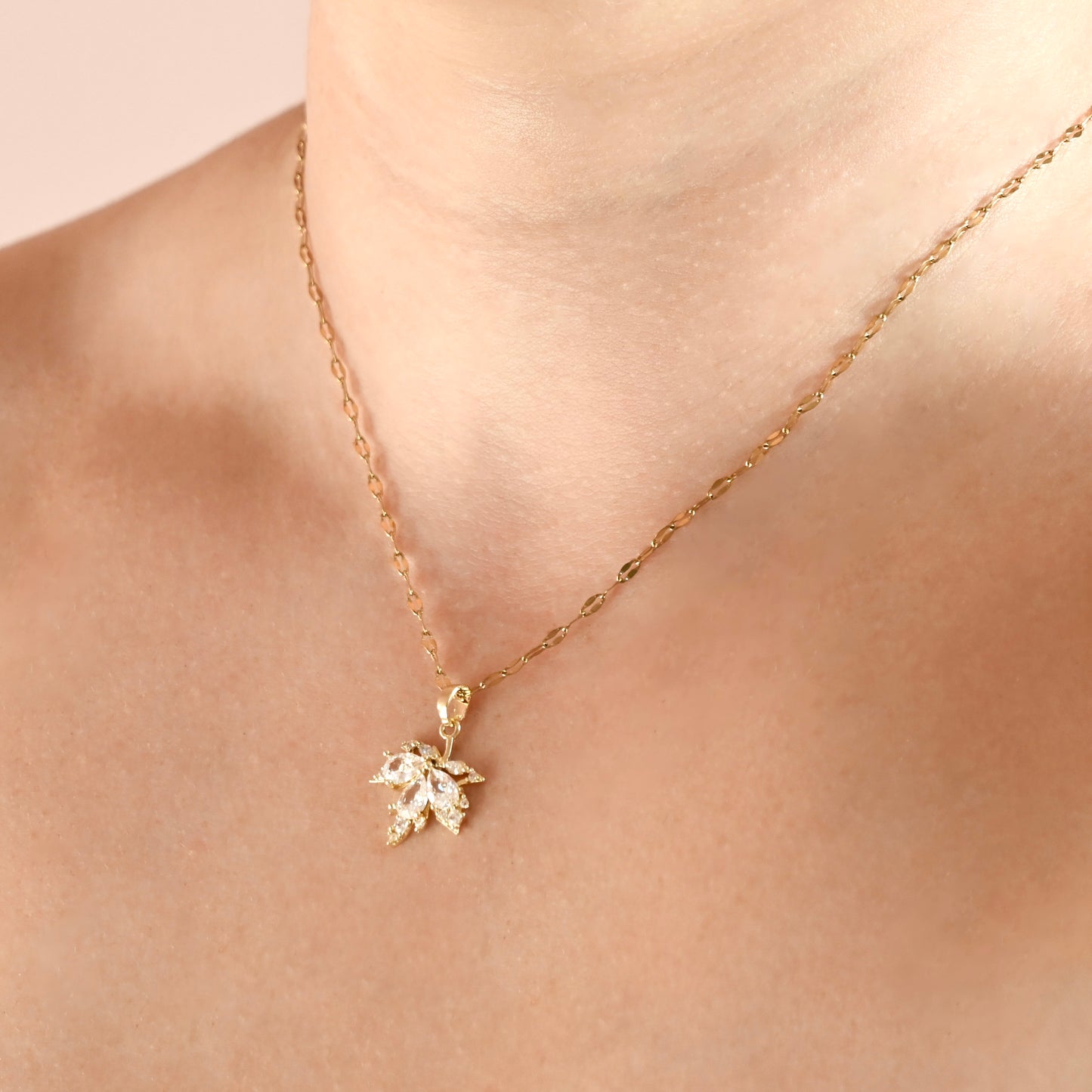 A delicate gold chain necklace with a small gold maple  leaf pendant adorned with clear crystals, shown worn on a model's neck.