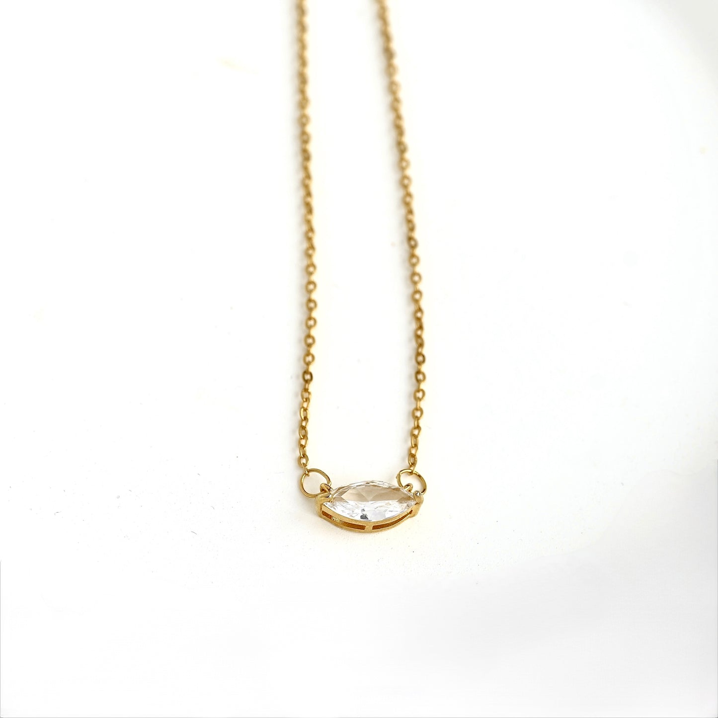 A delicate gold chain necklace with a small basket holding a marquise-cut clear gemstone with four prongs, displayed on a clean white background.