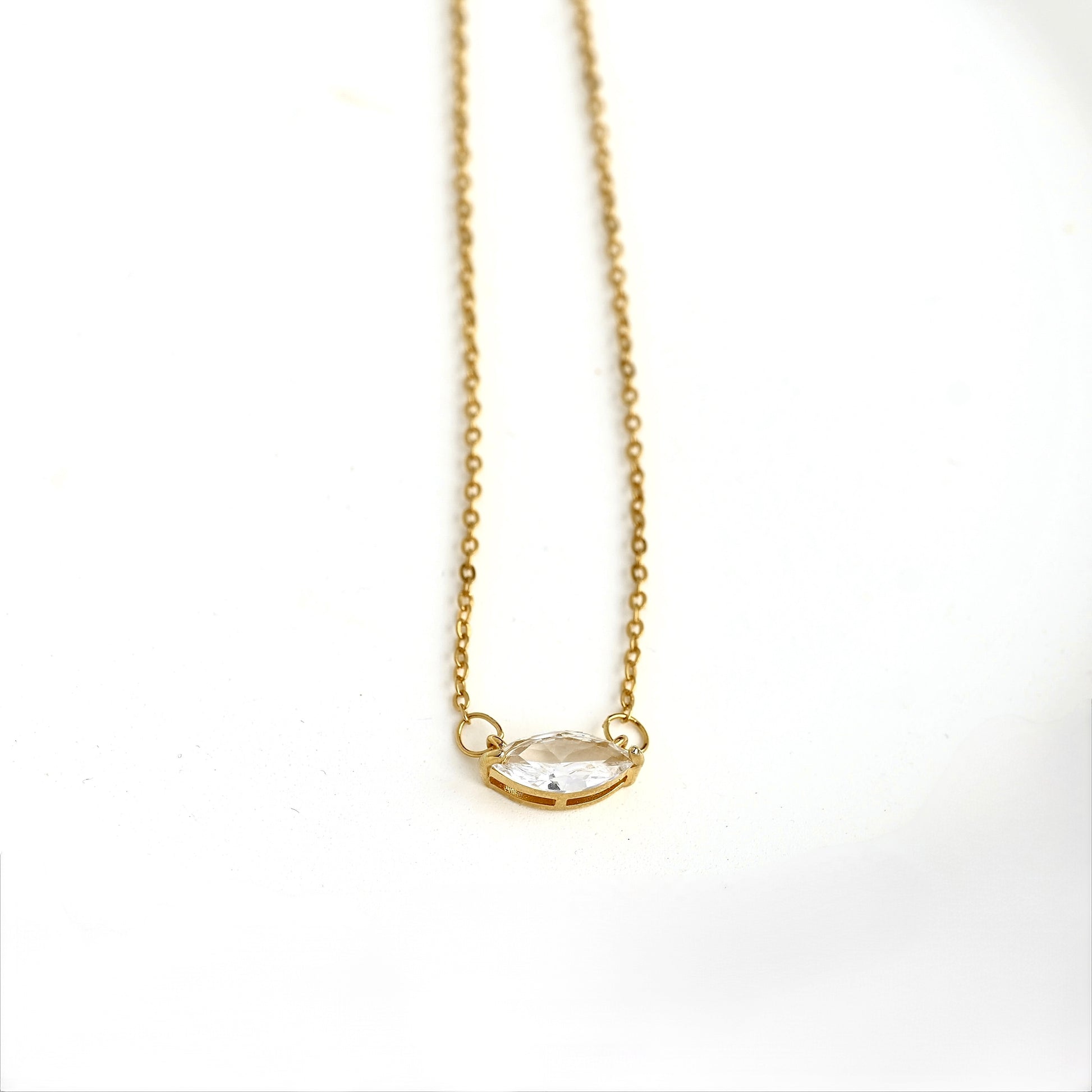 A delicate gold chain necklace with a small basket holding a marquise-cut clear gemstone with four prongs, displayed on a clean white background.