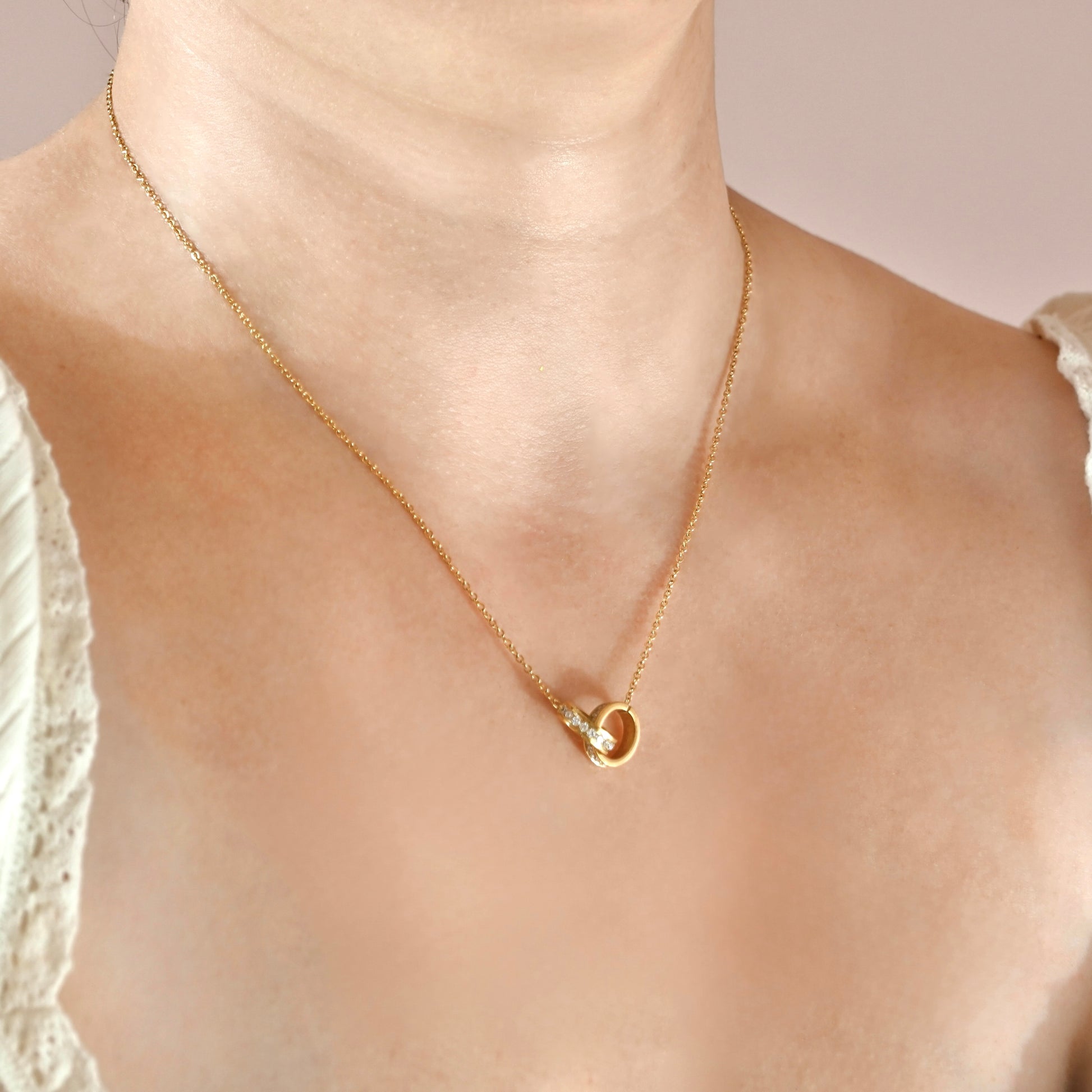 A delicate gold chain necklace with a small interlocking oval pendant, worn on a model's neck.