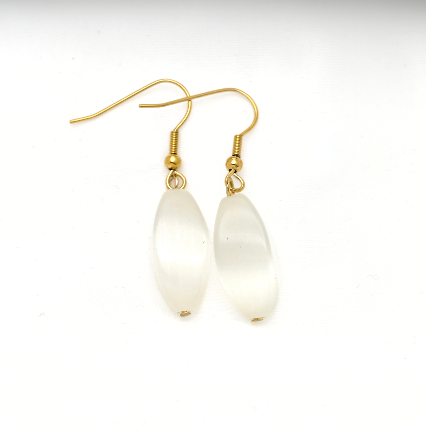 A pair of gold-tone dangle earrings with elongated, teardrop-shaped milky white cat eye stones, shown on a plain white background.