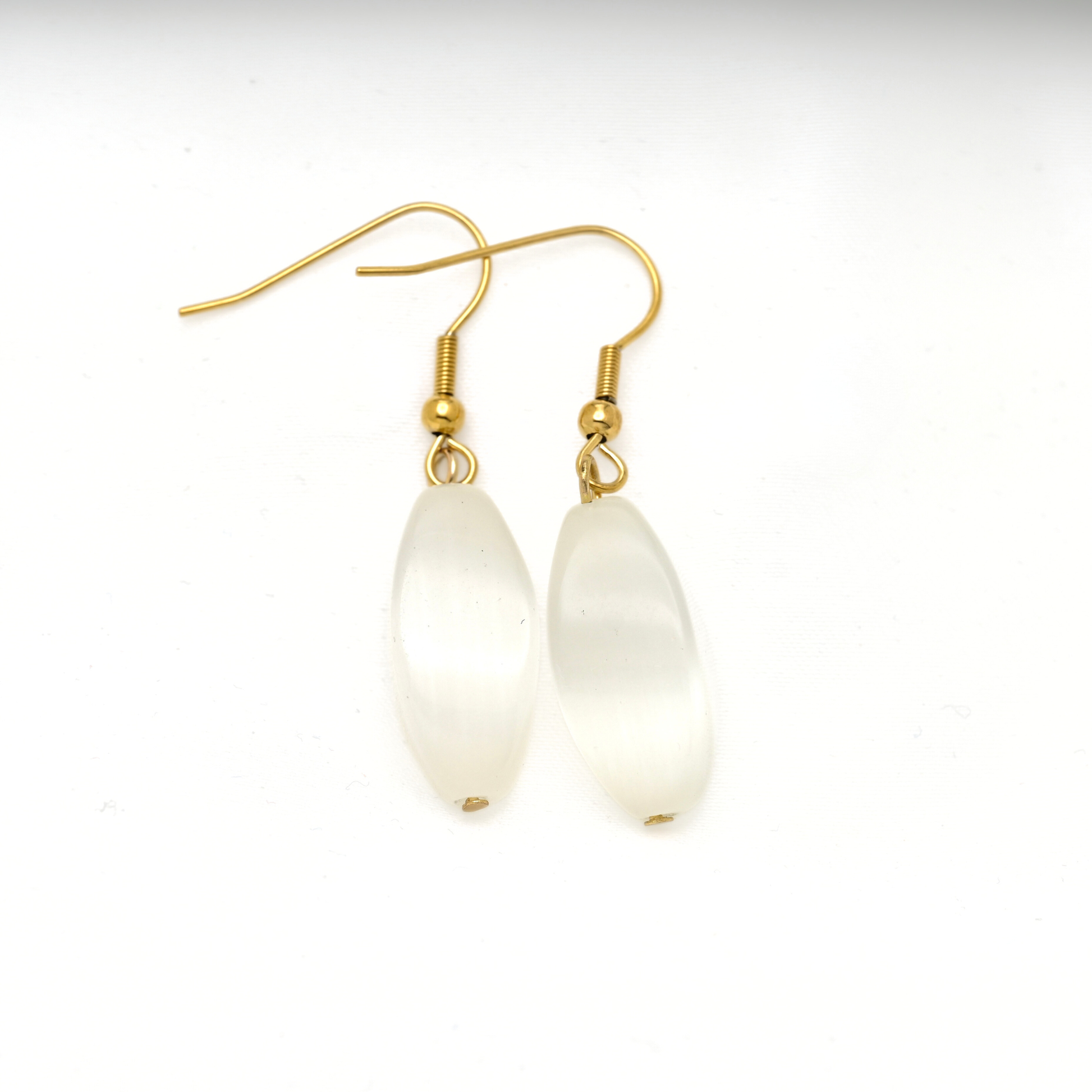 A pair of gold-tone dangle earrings with elongated, teardrop-shaped milky white cat eye stones, shown on a plain white background.