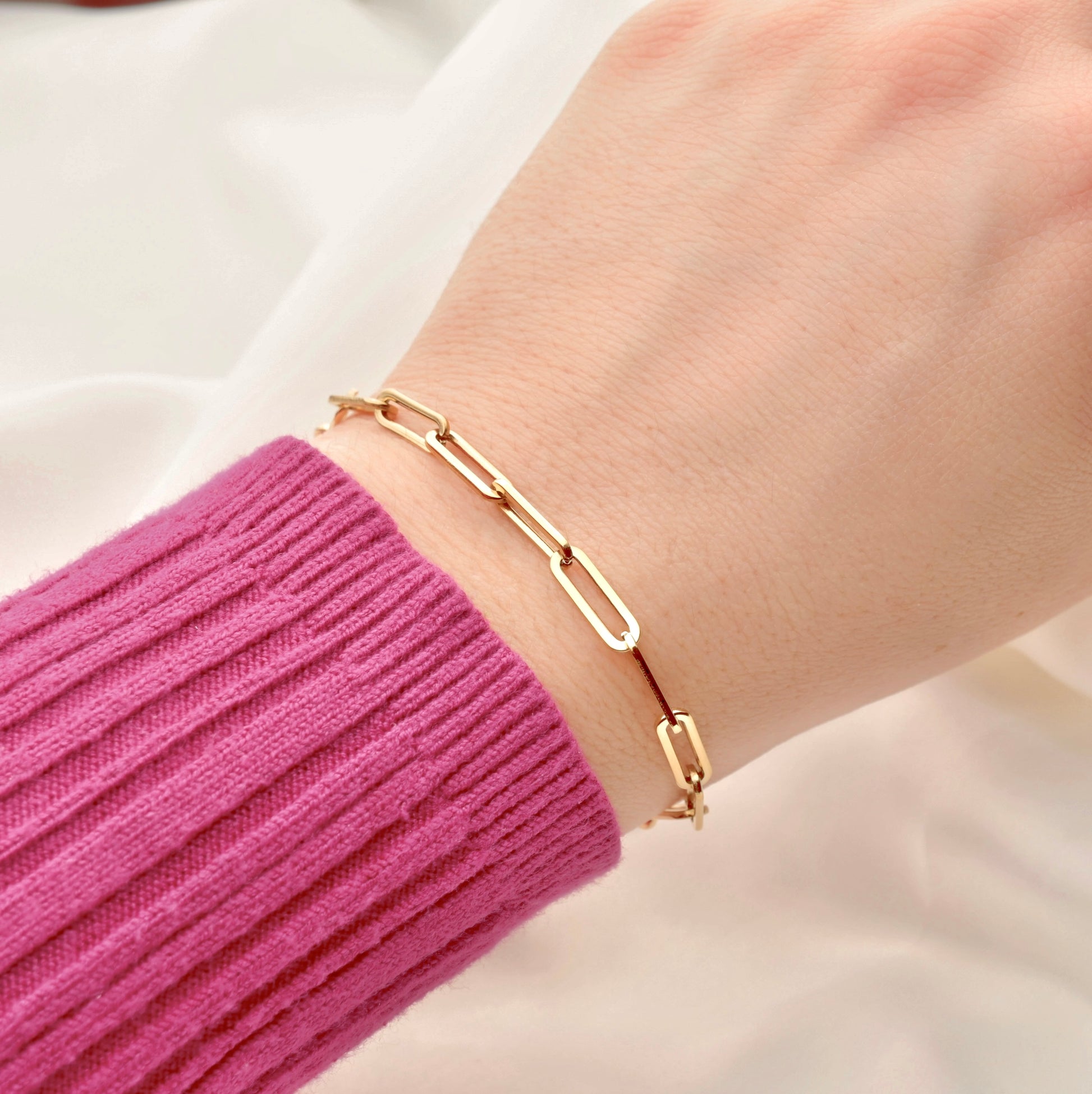 Top view of chunky gold bracelet on a wrist with a pink sleeve