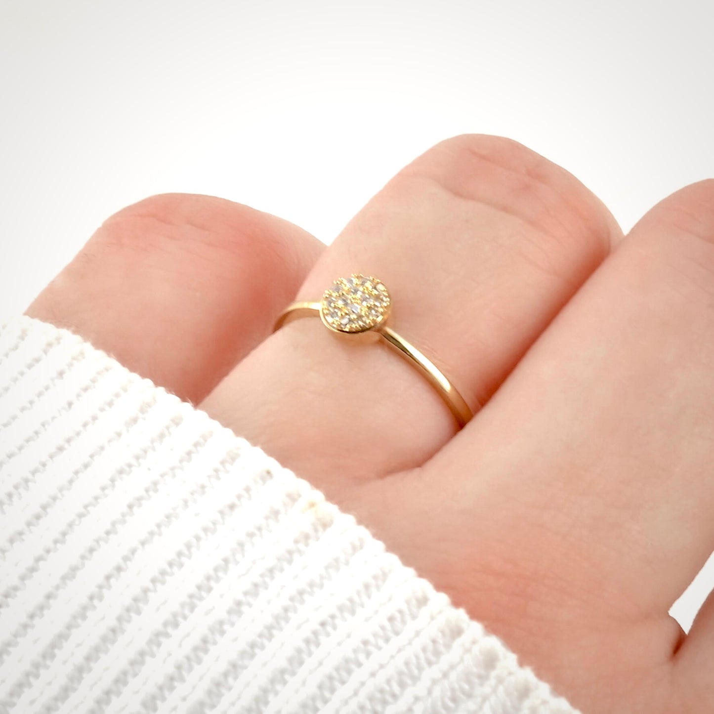 Gold circular ring with small diamonds on a finger against a white background