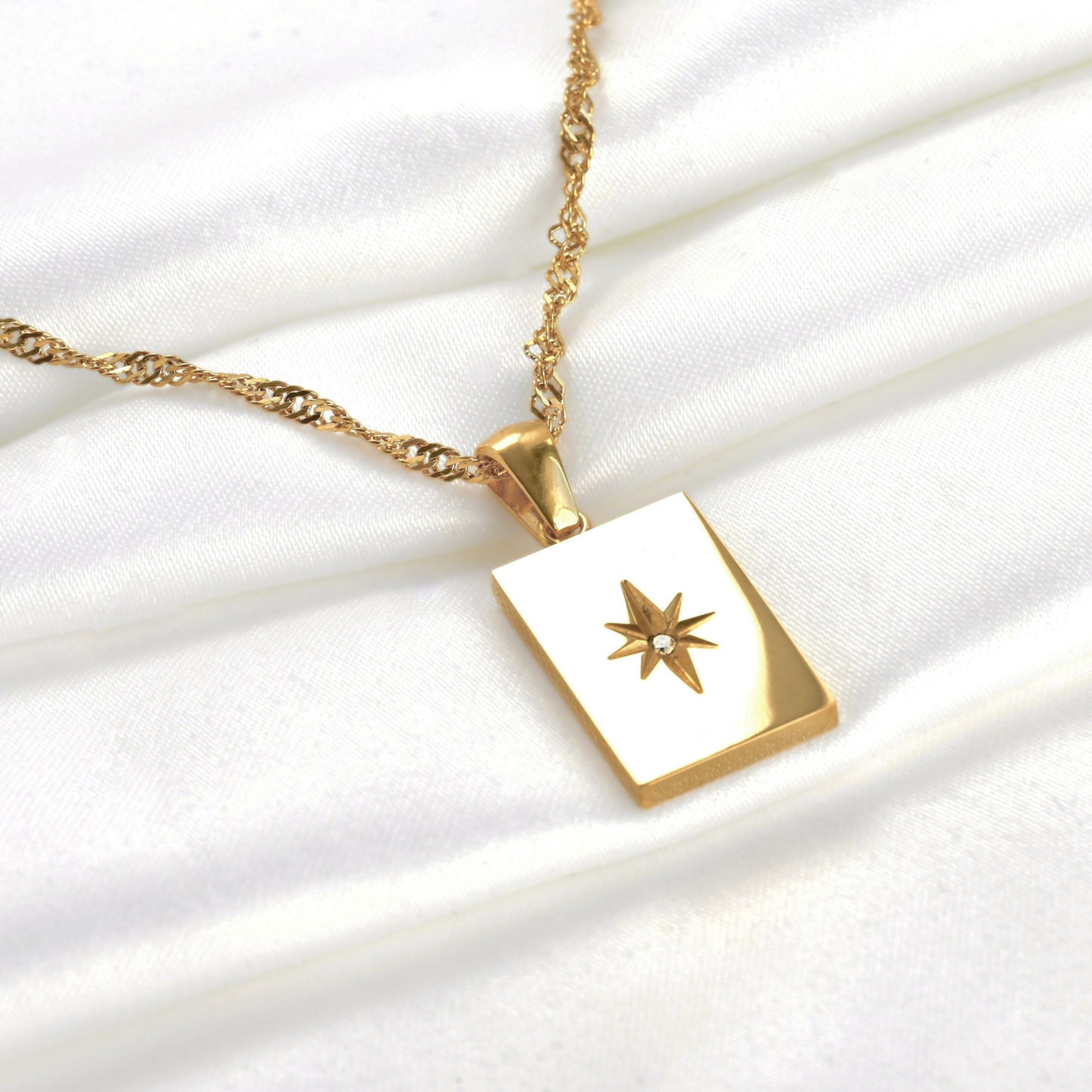 Front view of gold rectangle starburst necklace reflecting light on a white fabric background