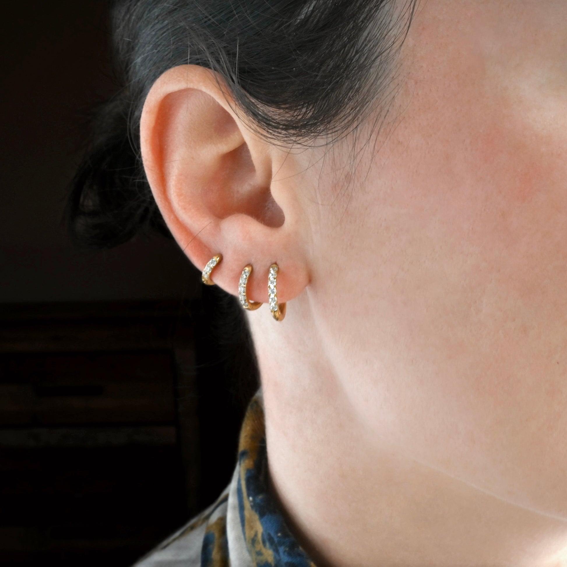 Close-up of an ear wearing a stack of of three half eternity gold hoop earrings in different sizes with a blurred background