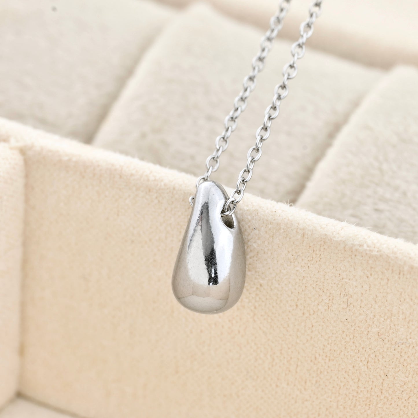 close up of Silver teardrop pendant necklace on a beige cushion