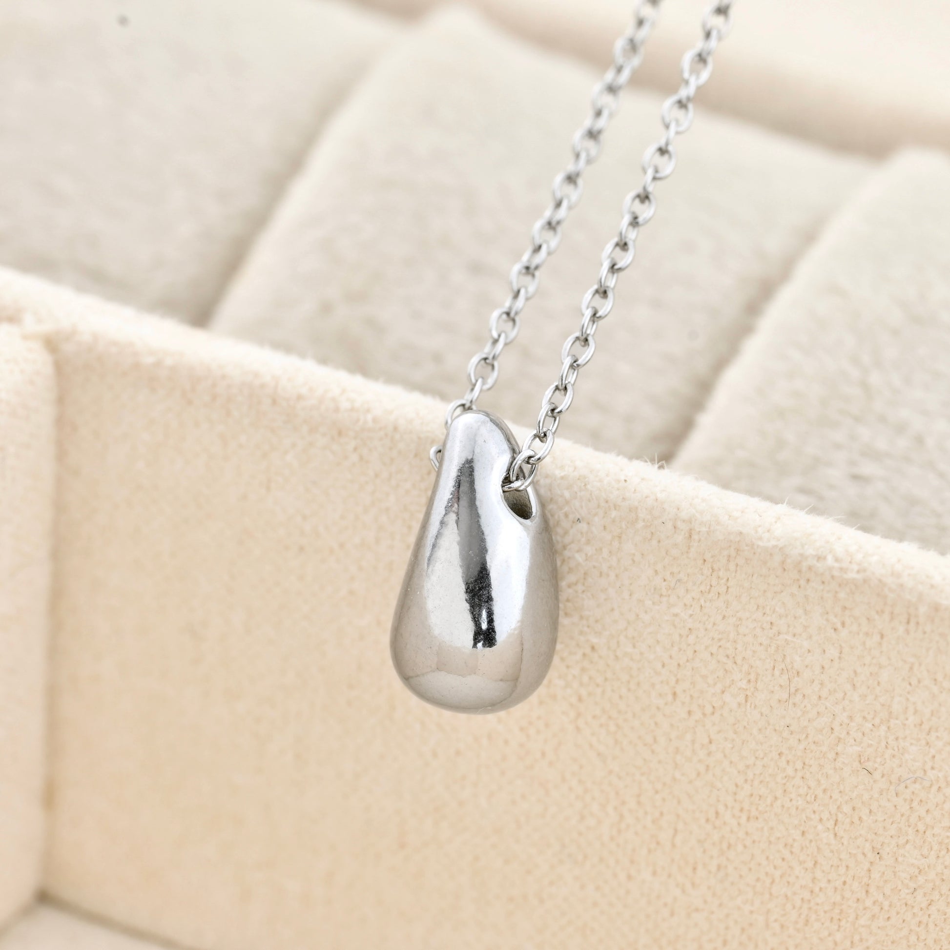 close up of Silver teardrop pendant necklace on a beige cushion