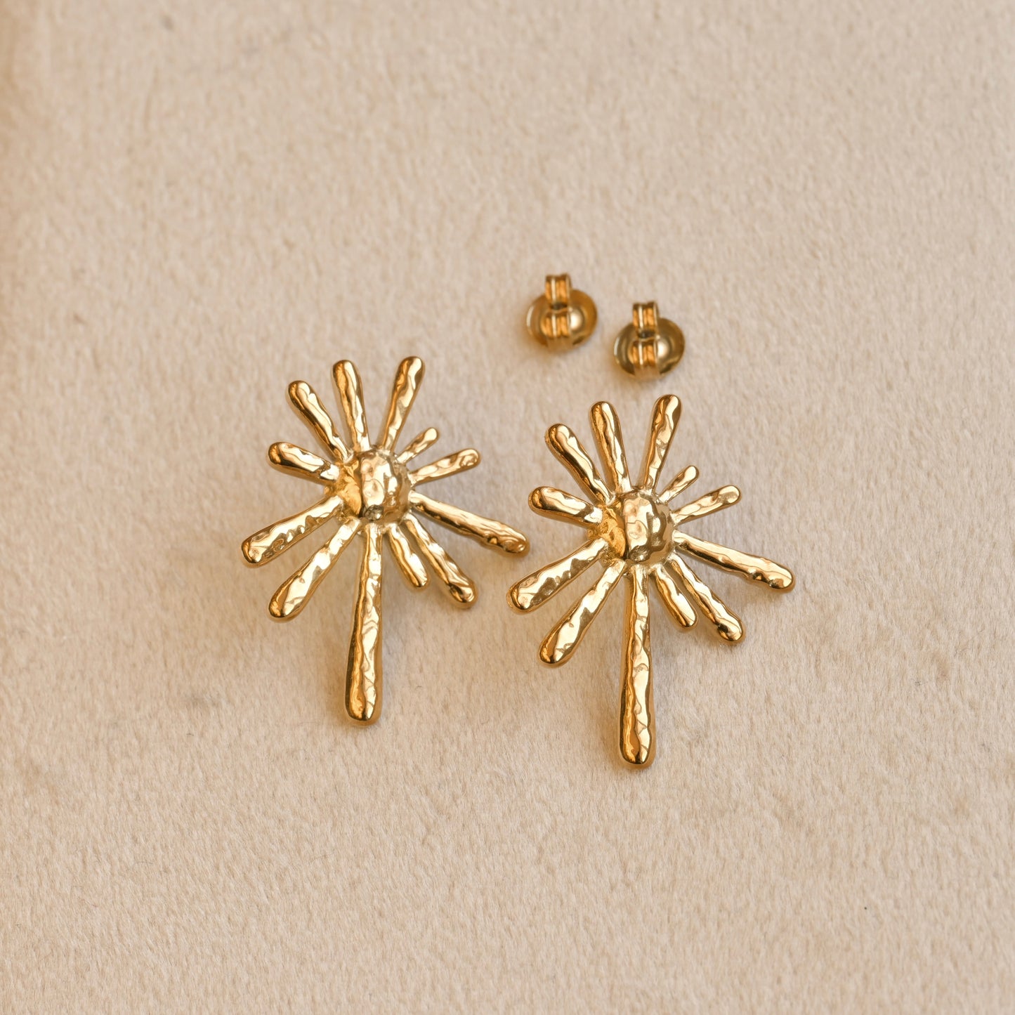 Gold starburst earrings on a beige background
