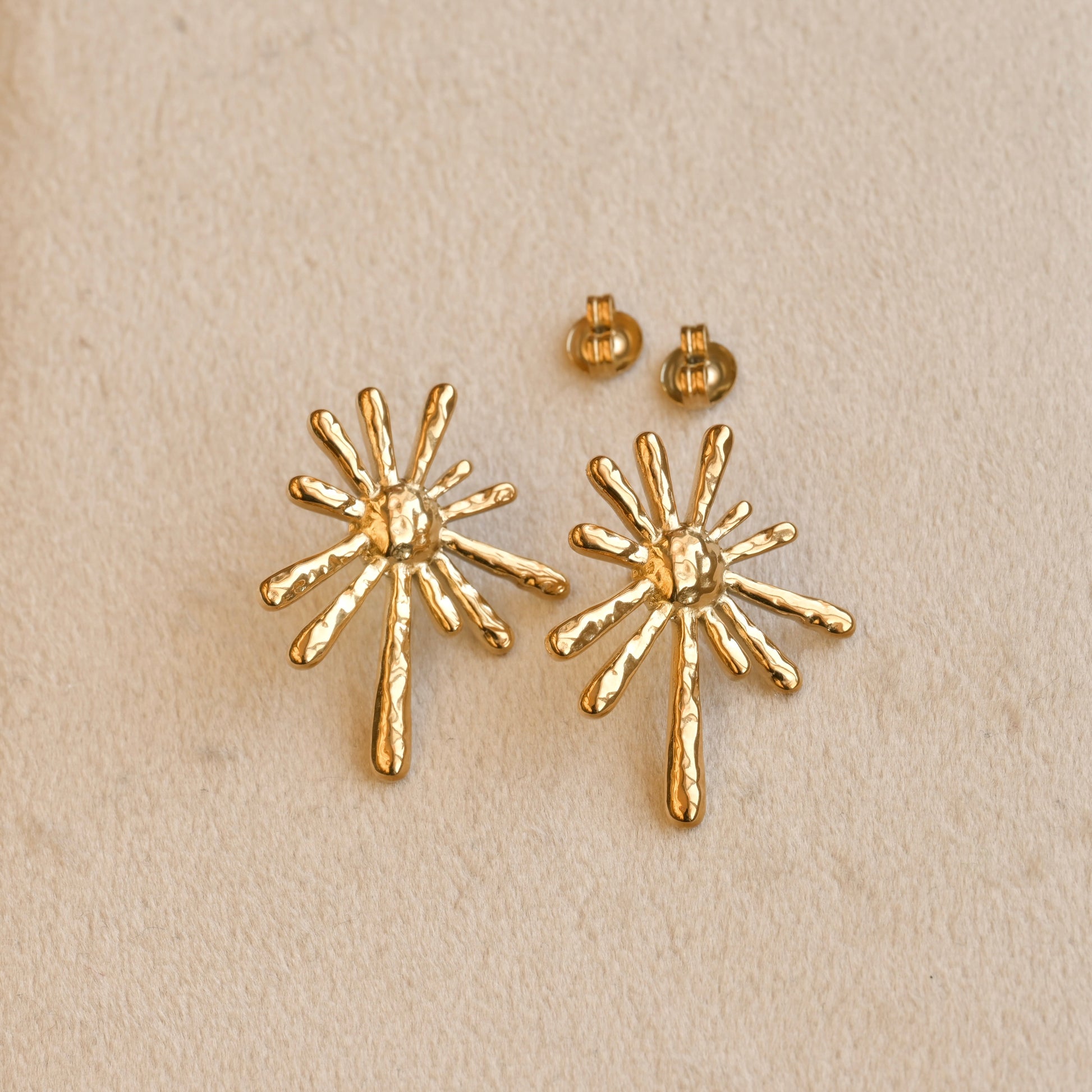 Gold starburst earrings on a beige background