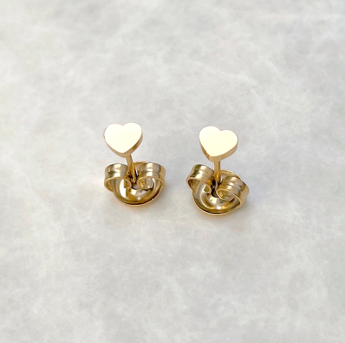 Top view of gold heart stud earrings on butterfly backs on a light gray background