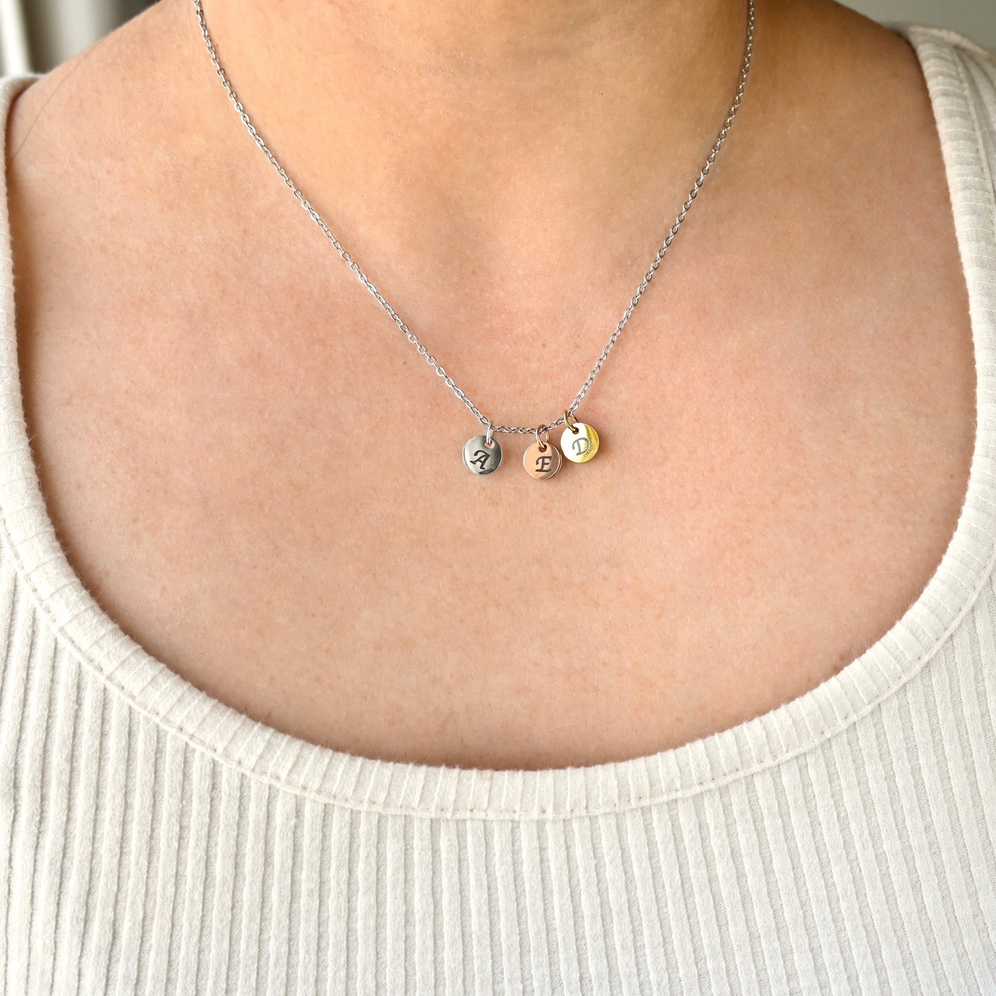 Necklace with three round letters on a person wearing a white top.