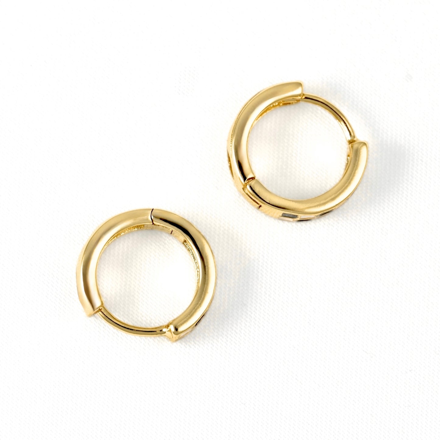 A pair of polished gold huggie hoop earrings on a clean white textured background.