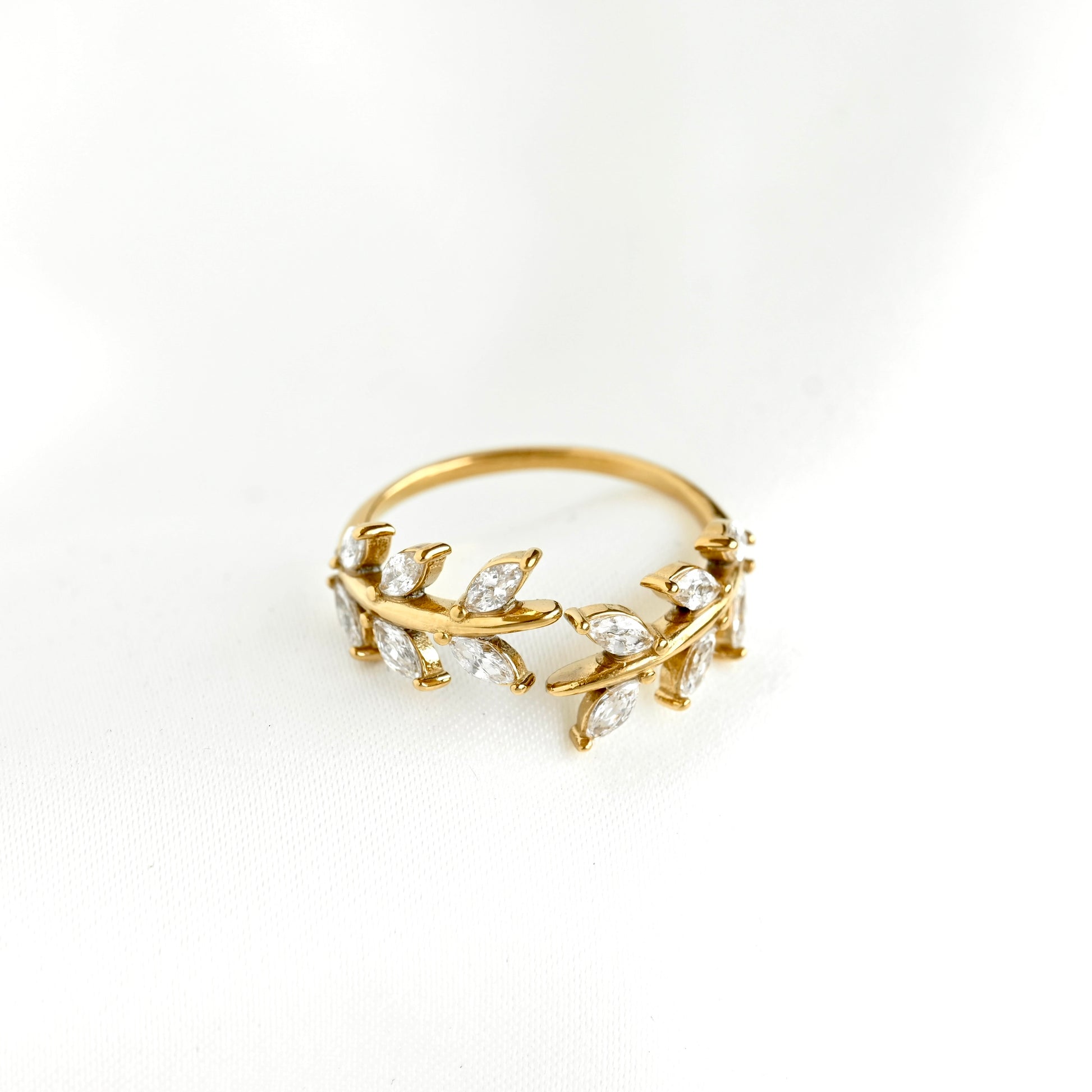 A gold ring featuring a delicate leafy vine design set with clear marquise-cut gemstones, photographed on a clean white background.