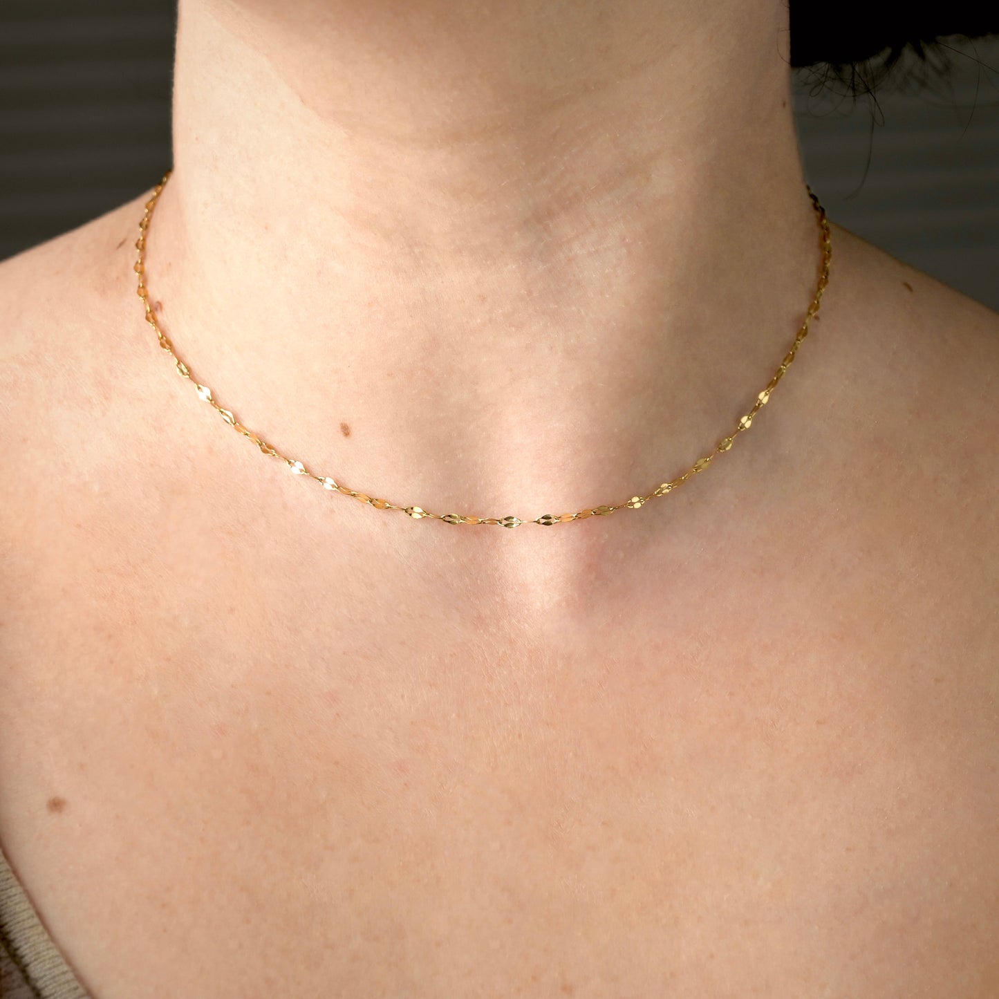 Sparkling gold sequin chain necklace on a person's neck with a blurred background